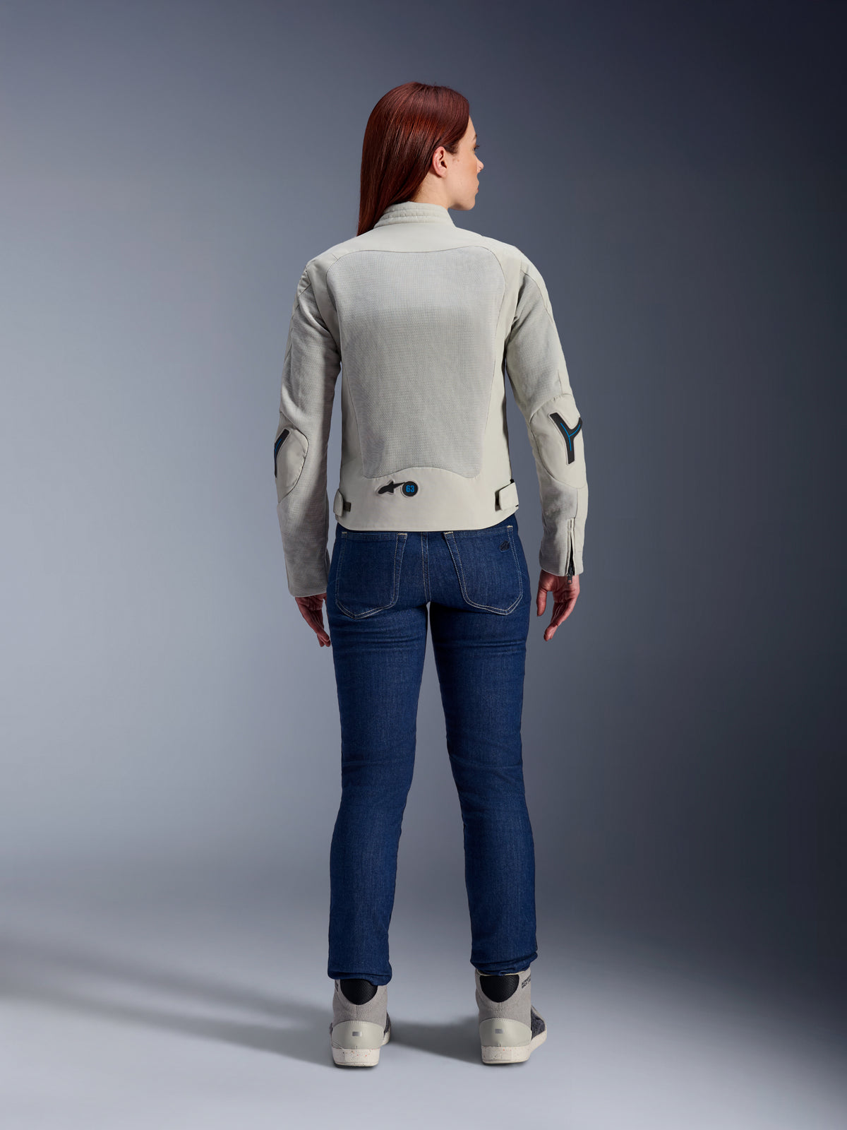 Alpinestars Woman Stella Circal-1 Air Jacket in Metal Gray and Methyl Blue, rear view, featuring large mesh airflow panels on the back and arms, worn with dark blue denim jeans and gray riding shoes for a modern urban motorcycle look.