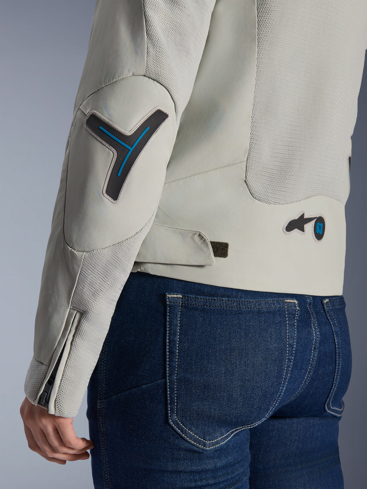 Alpinestars Woman Stella Circal-1 Air Jacket in Metal Gray and Methyl Blue, close-up of the back and sleeve detail showing mesh airflow panels, neon blue accents on the elbow and waist, and adjustable tab, worn with dark blue denim jeans.