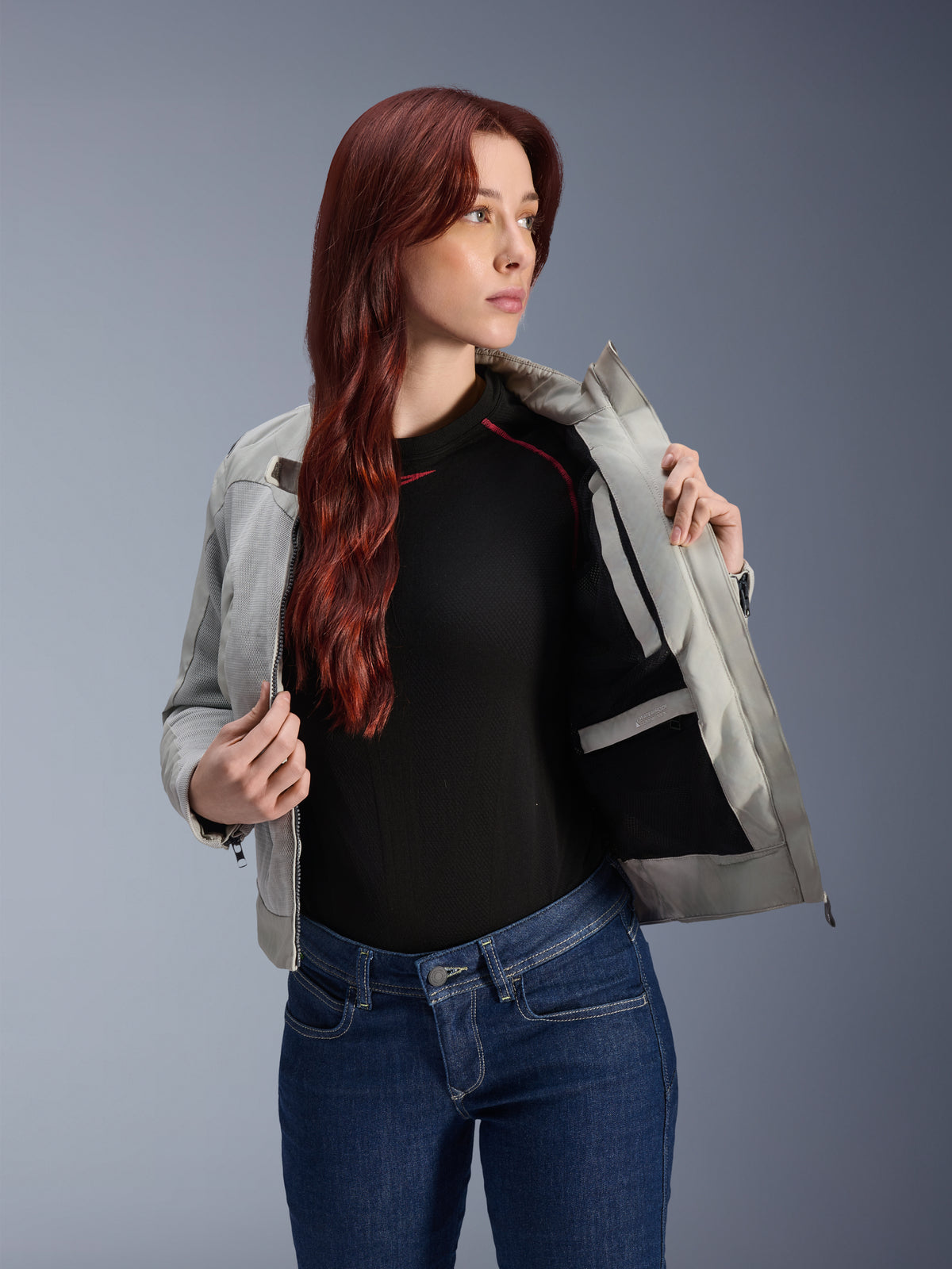 Alpinestars Stella Circal-1 Air Jacket in Metal Gray, female model opening the jacket to reveal the internal mesh lining and pocket, worn with blue jeans and a black top, contemporary urban motorcycle gear.