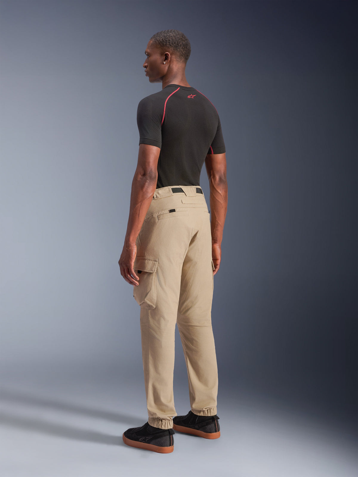 Alpinestars Flex-AST Cargo Pants - Short, Urban Motorcycle Pants in Light Beige, rear-quarter view showing side cargo pockets and elasticated hems, styled with a black short-sleeve top and black casual shoes