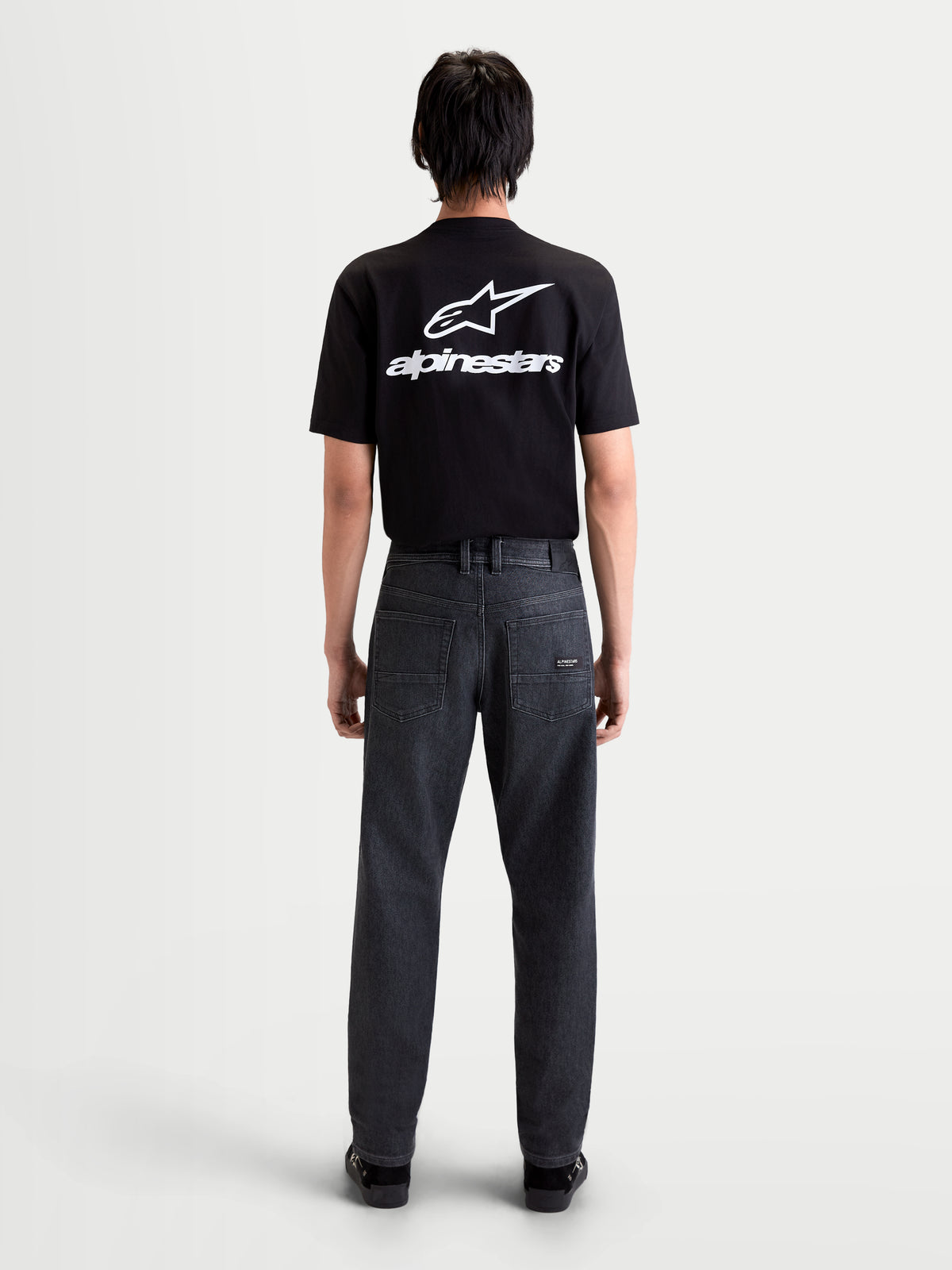 Alpinestars Flex-AST 7 Denim Pants, men's urban motorcycle riding jeans in faded black, rear view showing single-layer technical denim, five-pocket layout, and leather patch worn by a model.