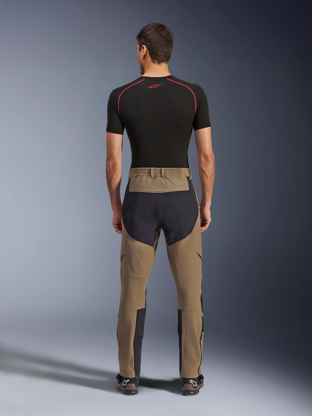 Alpinestars Flex-AST Explorer Pants, Walnut Black, rear view on model, featuring reinforced black seat and brown stretch textile, paired with black base layer and technical motorcycle boots, durable adventure riding apparel