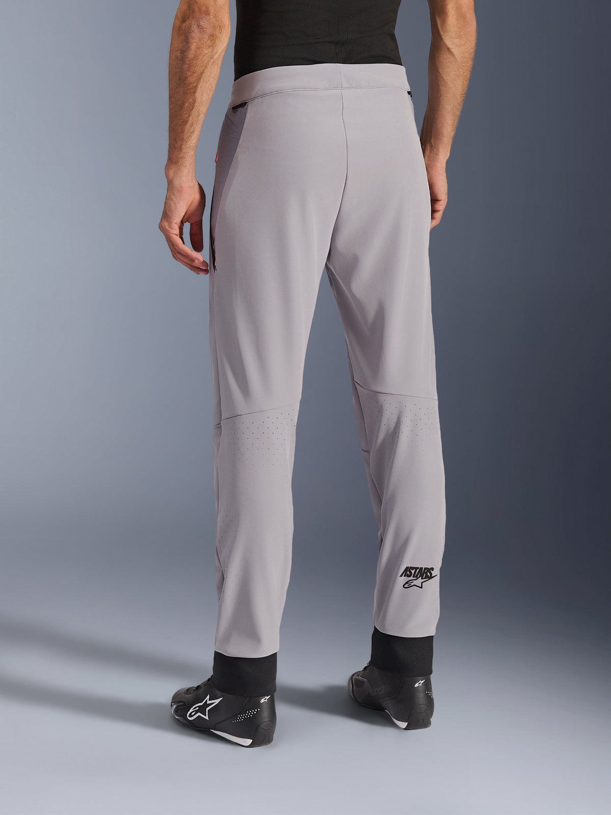 Alpinestars Aeroshell Airflow Pants, Mid Gray, back view showing laser-perforated zones on the calves, ASTARS logo on the lower leg, black adjustable ankle cuffs, worn with black motorcycle boots, lightweight sport riding textile pants