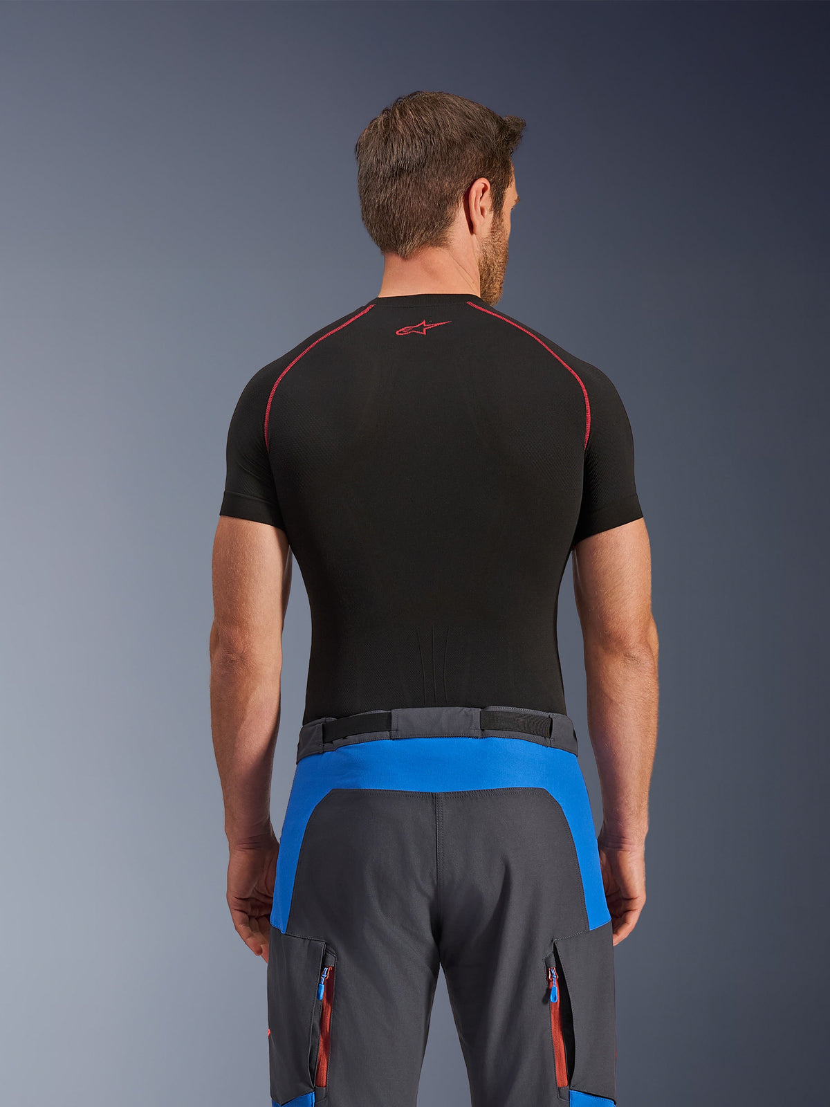 Alpinestars Maxdura Dual Pants, Adventure Motorcycle Pants, Royal Blue and Deep Gray, rear view, worn with a black short-sleeve base layer, featuring blue accent panels on the upper back and orange zippered cargo pockets, technical outdoor gear for dual-sport riding