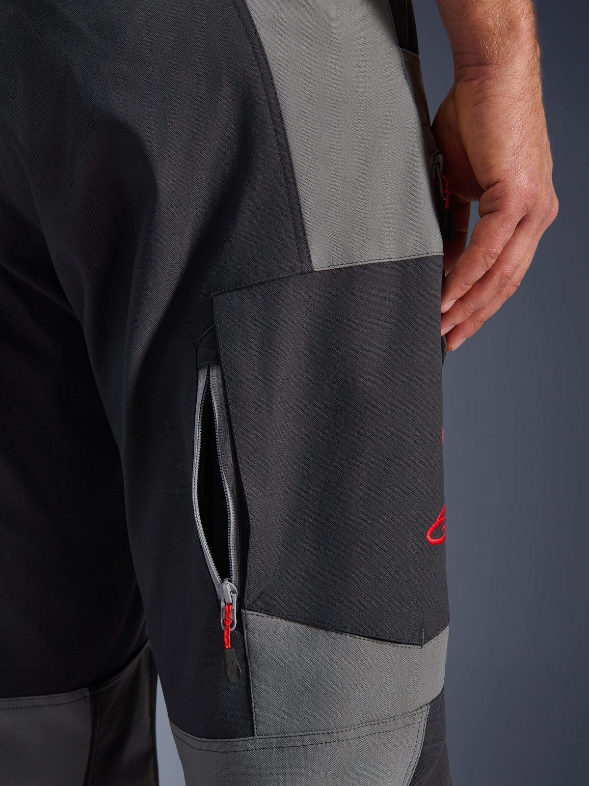 Alpinestars Maxdura Dual Pants, adventure motorcycle pants in Dark Gray and Deep Gray, close-up of the thigh featuring a zippered ventilation vent and red embroidered logo, durable stretch polyamide construction.