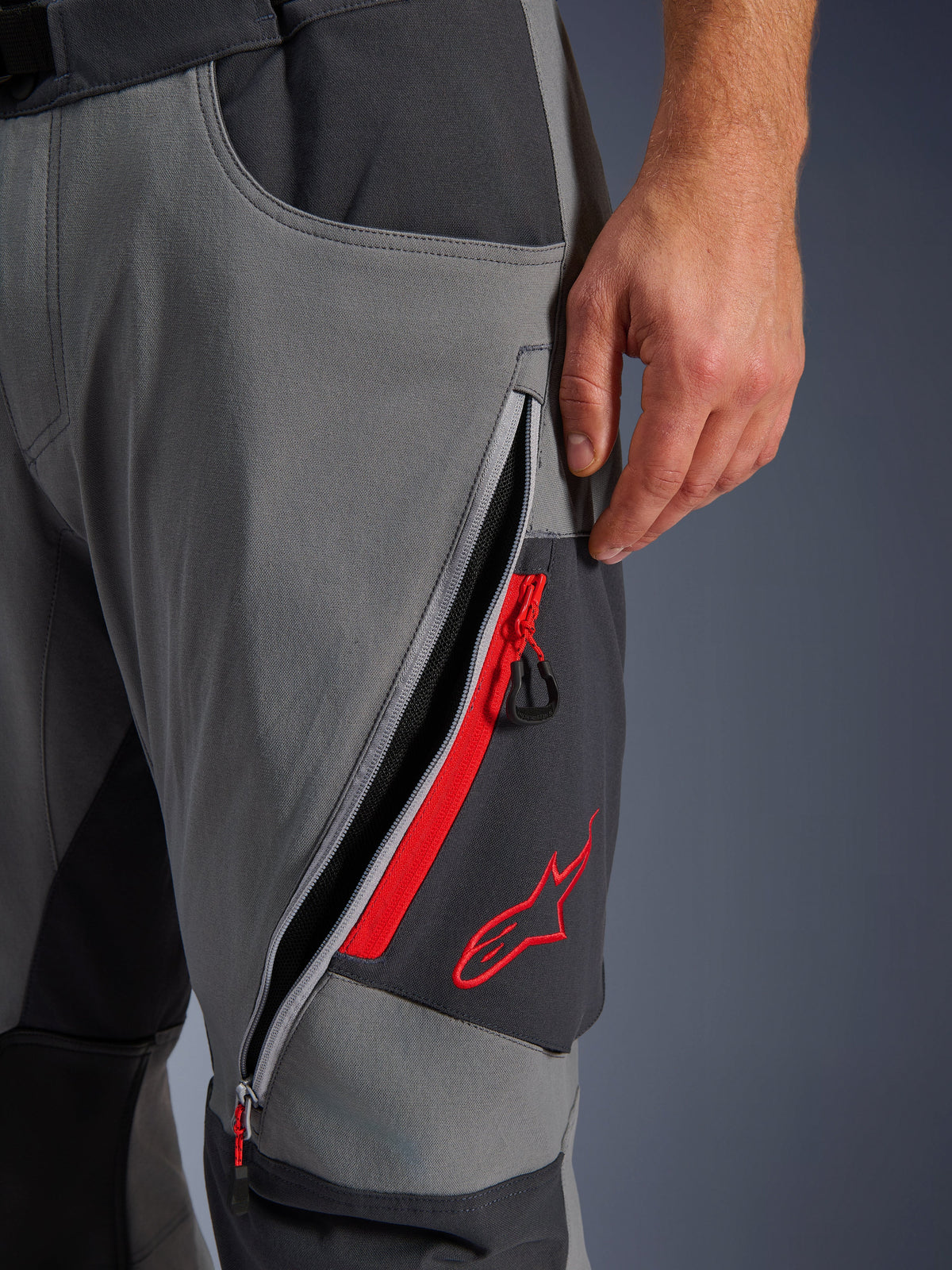Alpinestars Maxdura Dual Pants, Dark Gray and Deep Gray adventure motorcycle pants, close-up view of open zippered thigh vent with red highlights and embroidered red star logo, technical stretch fabric design