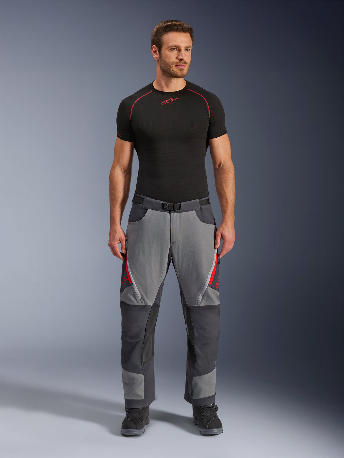 Alpinestars Maxdura Dual Pants, Motorcycle Pants, Dark Gray and Deep Gray with red accents, front view worn by a model with a black Alpinestars base layer and black boots, featuring reinforced panels and zippered thigh vents, adventure-style riding gear