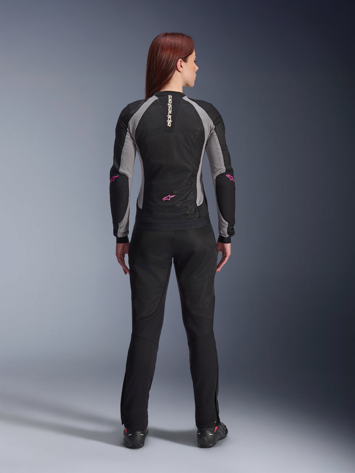Woman Stella Troop-Air Jacket and matching pants seen from behind, Black Ash Gray and Pink Fluo, lightweight mesh motorcycle gear with gray panels and pink fluo accents, featuring vertical Alpinestars branding and star logos.
