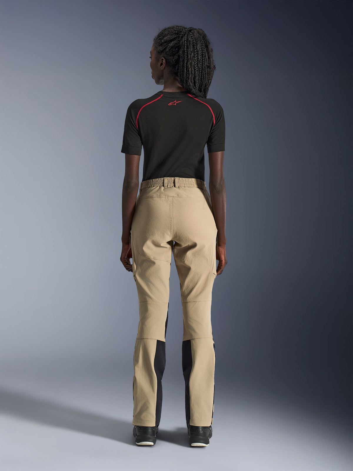 Alpinestars Woman Stella Flex-AST Explorer Pants in Sand, rear view on a model, paired with a black short-sleeved base layer and black boots, featuring reinforced seat panels and ergonomic textile construction for adventure touring.