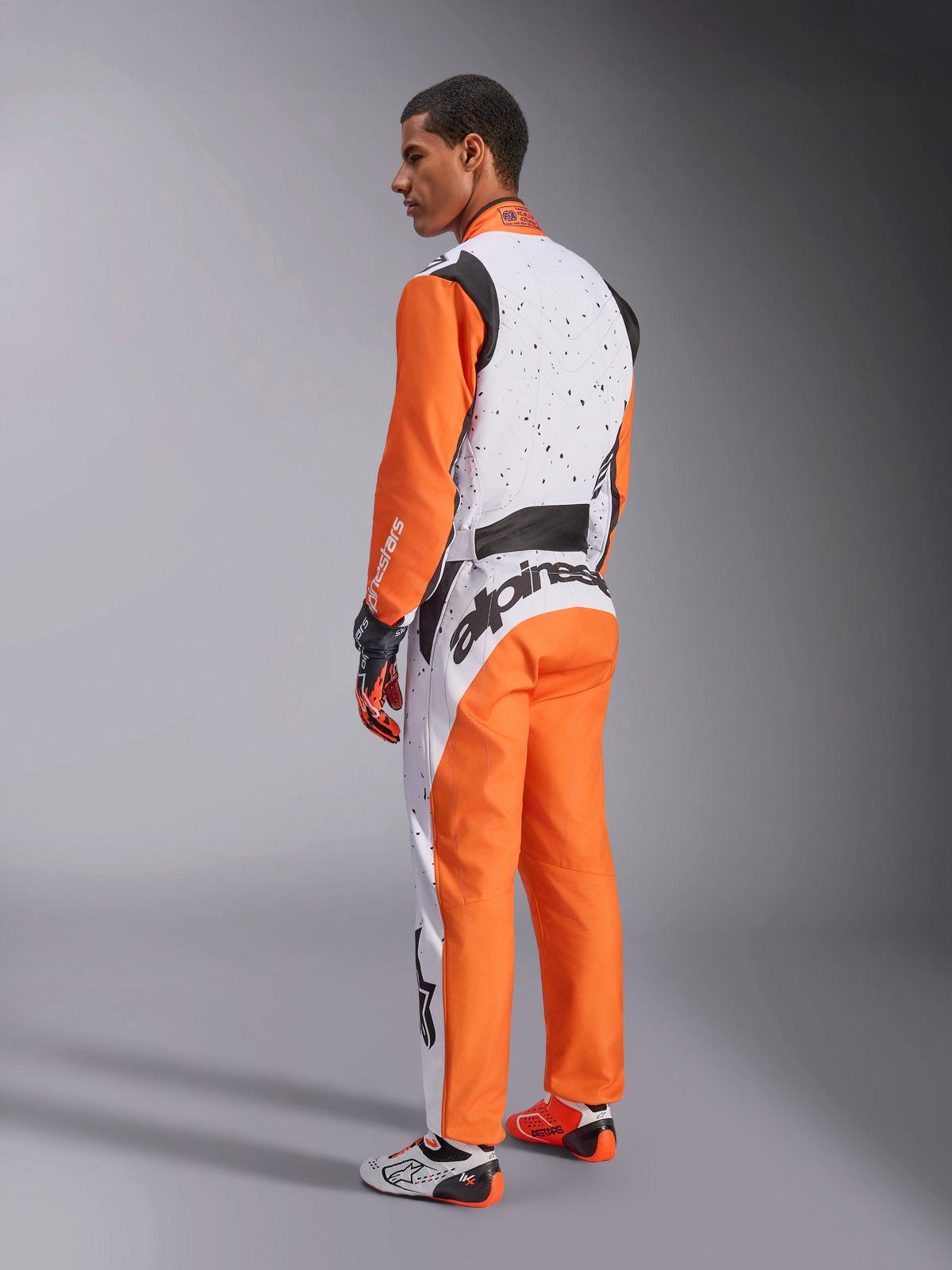Alpinestars KMX-9 V3 Graphic 6 Suit, Karting Suit, White Orange and Black, back view showing white torso with black splatter graphics, orange sleeves and pants, large black branding on lower back, complete with matching gloves and racing footwear