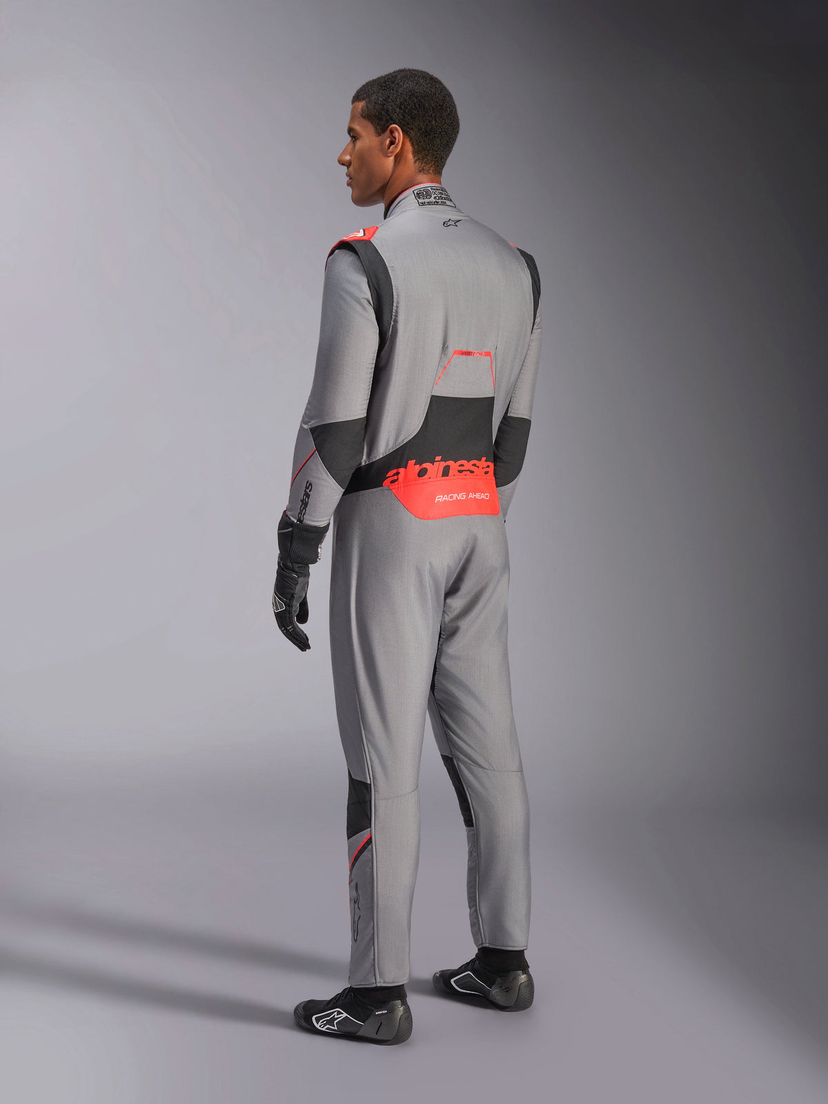 Alpinestars Hypertech V3 Suit in Mid Gray Black Red Fluo, rear three-quarter view, featuring bold red Alpinestars branding on the lower back, black stretch panels, and a sleek athletic fit for professional auto racing.