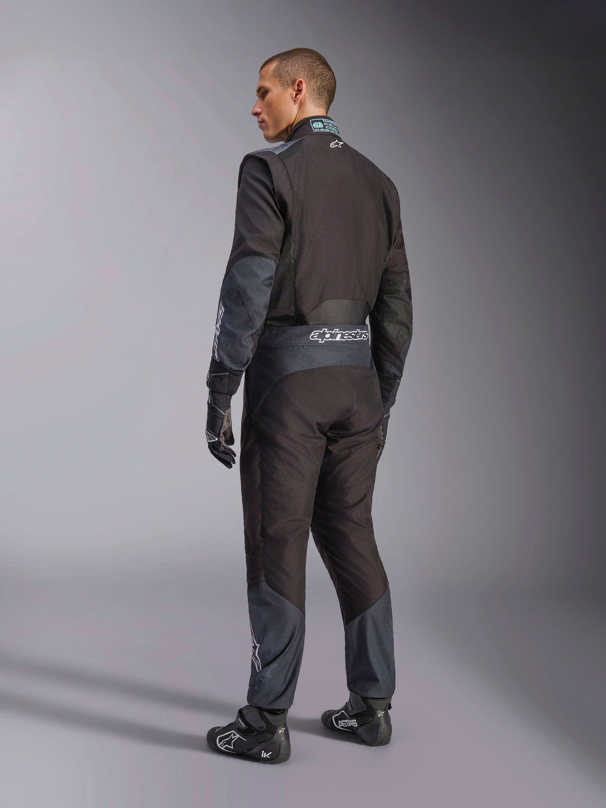 Alpinestars KMX-5 V3 Suit in Black Dark Shadow, rear view of model wearing full karting gear including matching gloves and racing shoes, featuring Alpinestars branding on the waist and dark shadow accents, professional karting gear.