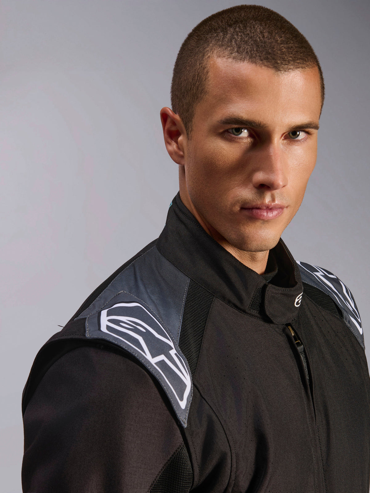 Male model wearing Alpinestars KMX-5 V3 Suit, Black Dark Shadow karting suit, close-up view of the chest and shoulder area, featuring grey accents and white Astars logos, professional motorsport protective gear