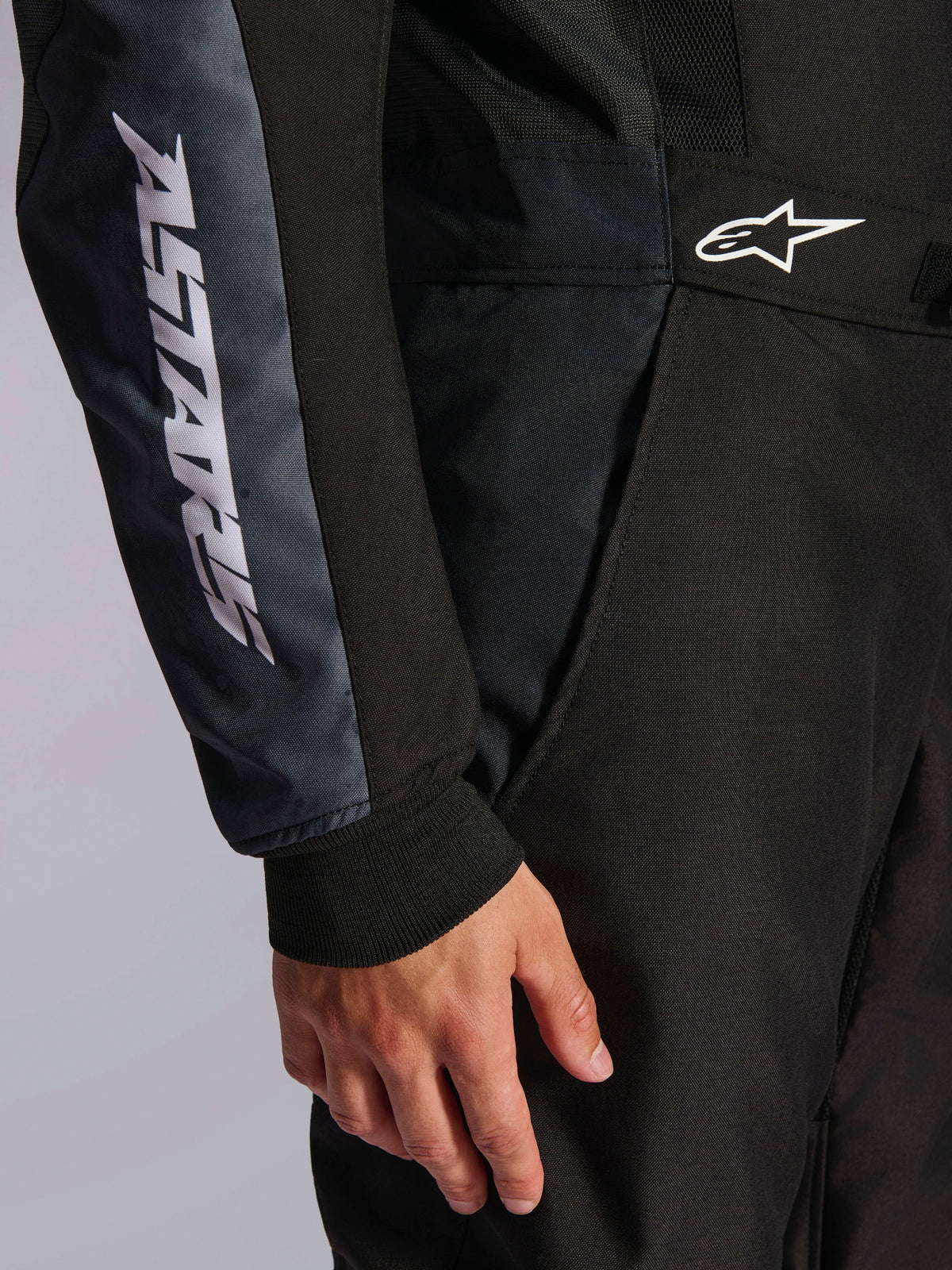 Alpinestars KMX-5 V3 Suit, Karting Suit, Black and Dark Shadow, close-up detail of side hip and arm, white ASTARS branding on the sleeve, white logo on the waist, featuring mesh panels for ventilation and a knitted wrist cuff