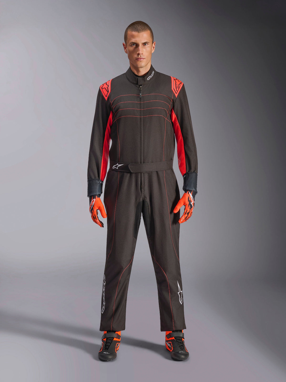 Alpinestars KMX-9 V3 Karting Suit, Black and Red Fluo, one-piece racing suit worn with coordinating gloves and boots, featuring vibrant red shoulder accents and stitching, Alpinestars logo on lower legs, sleek motorsport design for track racing