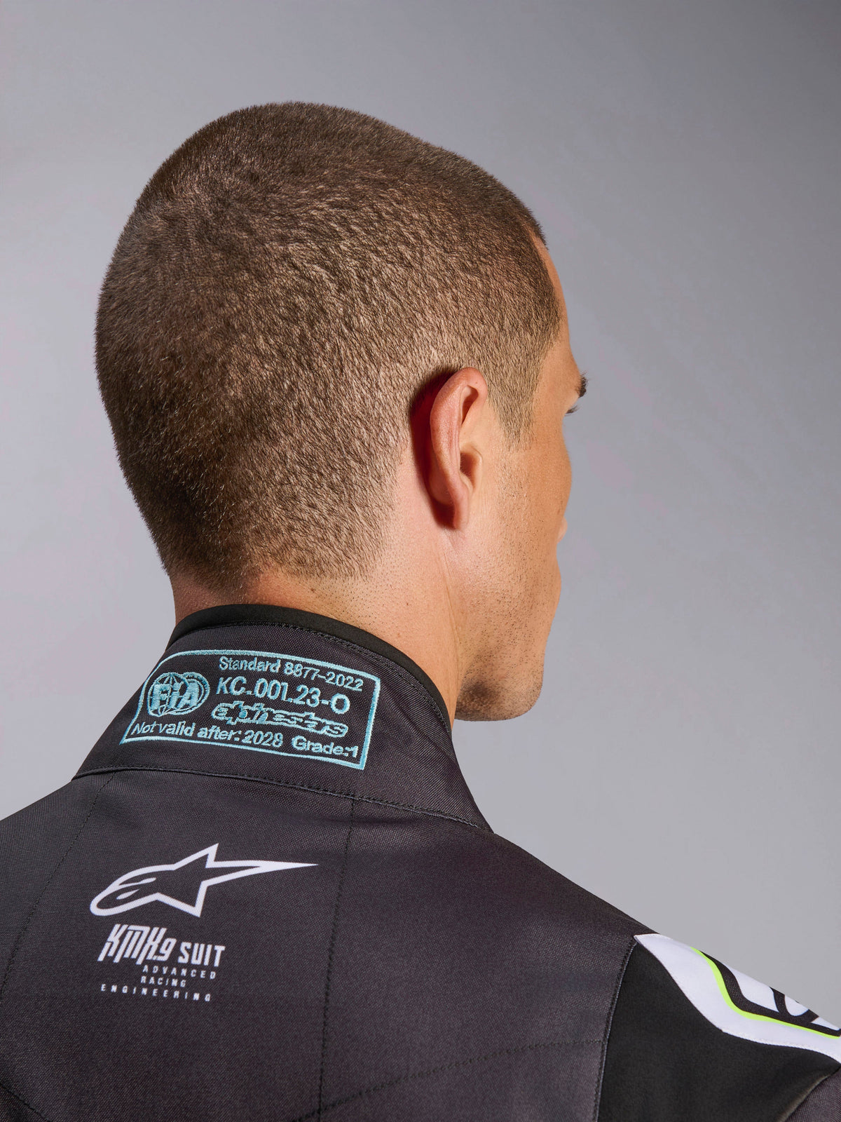 Alpinestars KMX-9 V3 Graphic 3 Suit, close-up of the back collar area, showing the FIA 8877-2022 Grade 1 homologation label and white KMX-9 branding on black material, karting racing gear detail