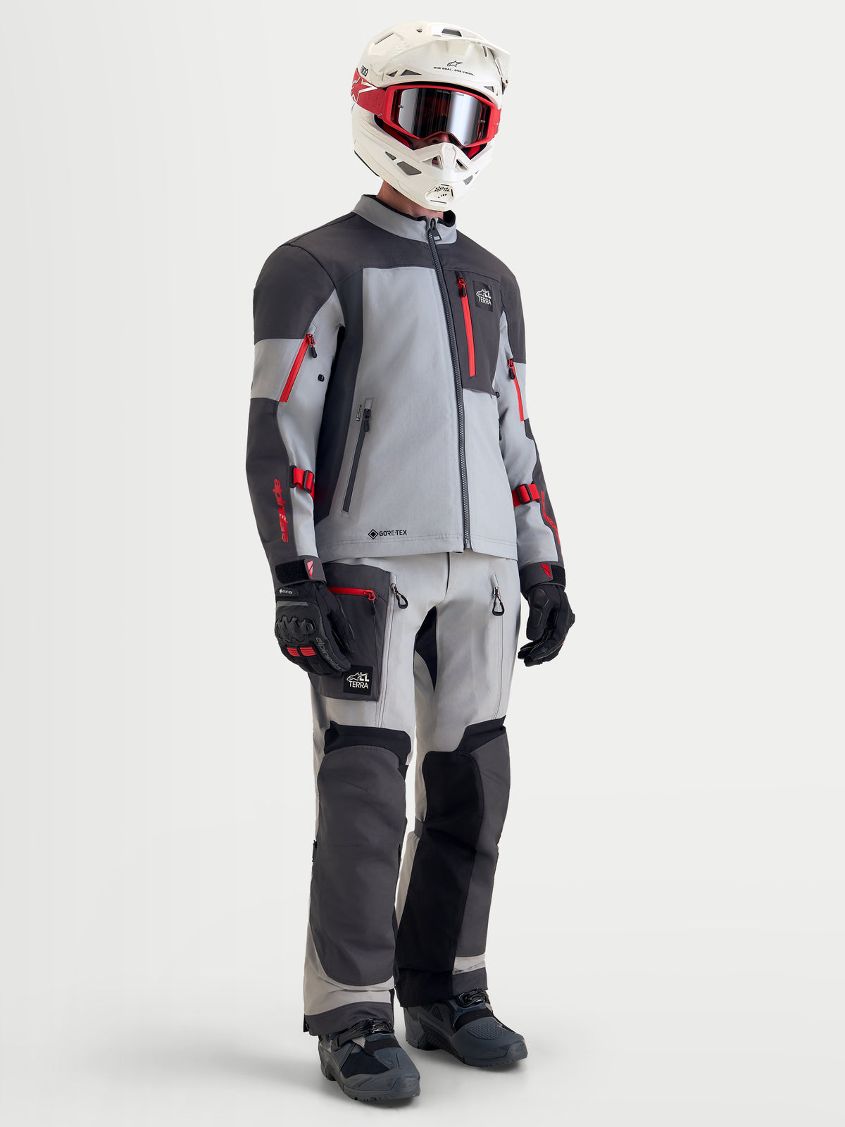 Alpinestars Arenis Gore-Tex Gear Set, men's adventure touring motorcycle jacket and pants in gray, dark gray, and red, full-body view on a model wearing matching helmet, goggles, gloves, and boots, waterproof all-terrain riding apparel.