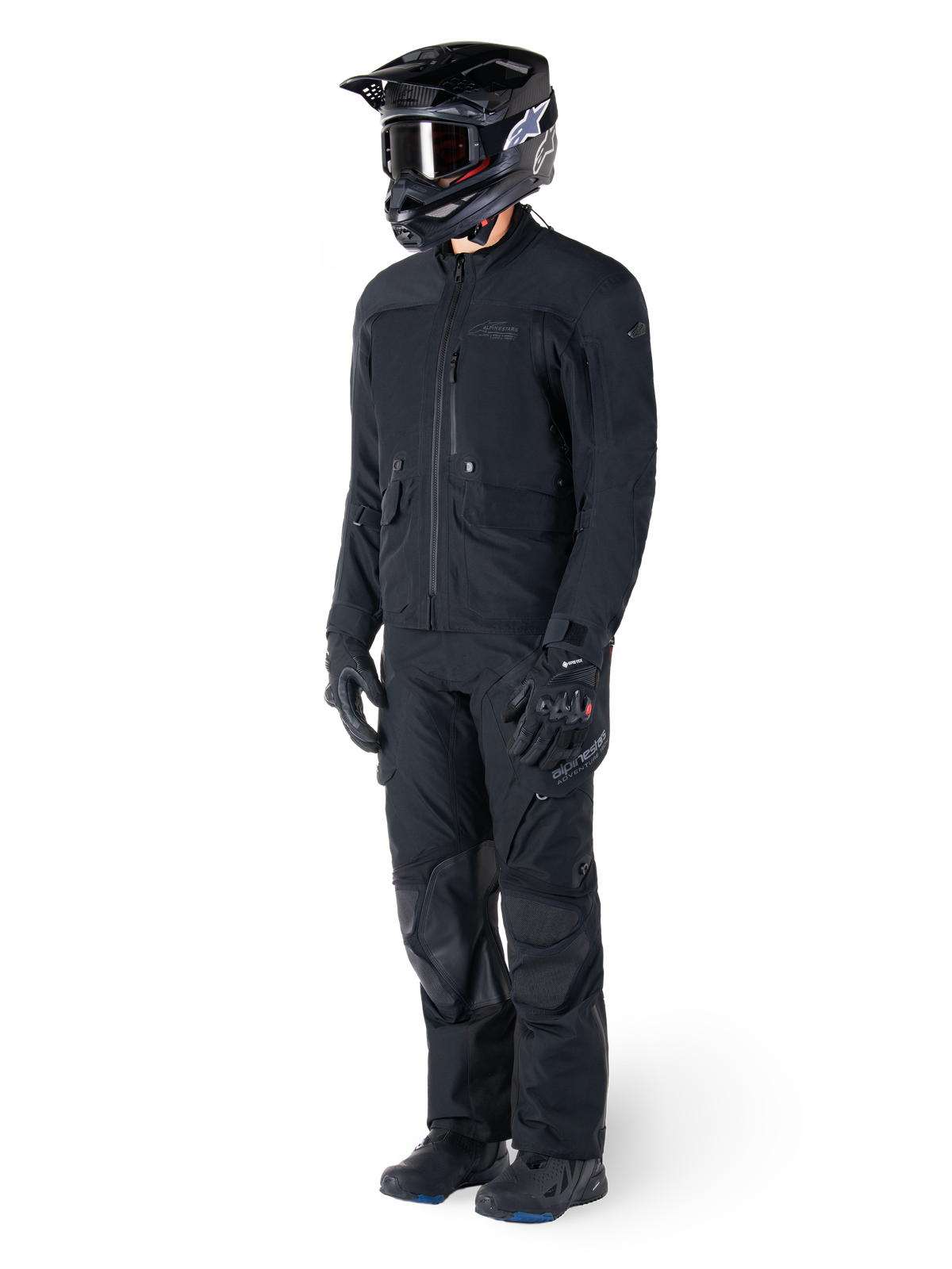 Motorcyclist wearing the Alpinestars St-7 Prime GORE-TEX Jacket in black, coordinated adventure touring outfit with matching black pants, black helmet with goggles, and gloves, featuring a streamlined and functional design for all-weather performance.