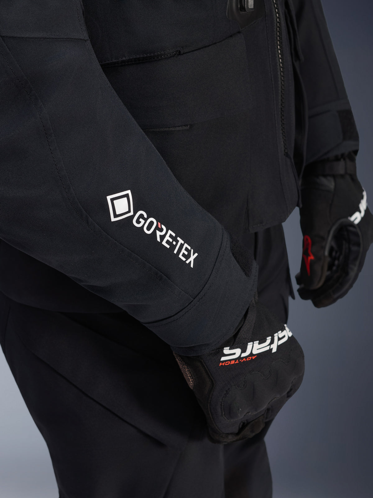 Alpinestars ST-7 2L GORE-TEX Jacket, Black and Dark Gray, close-up of sleeve featuring white GORE-TEX branding, worn with black adventure riding gloves, waterproof motorcycle apparel