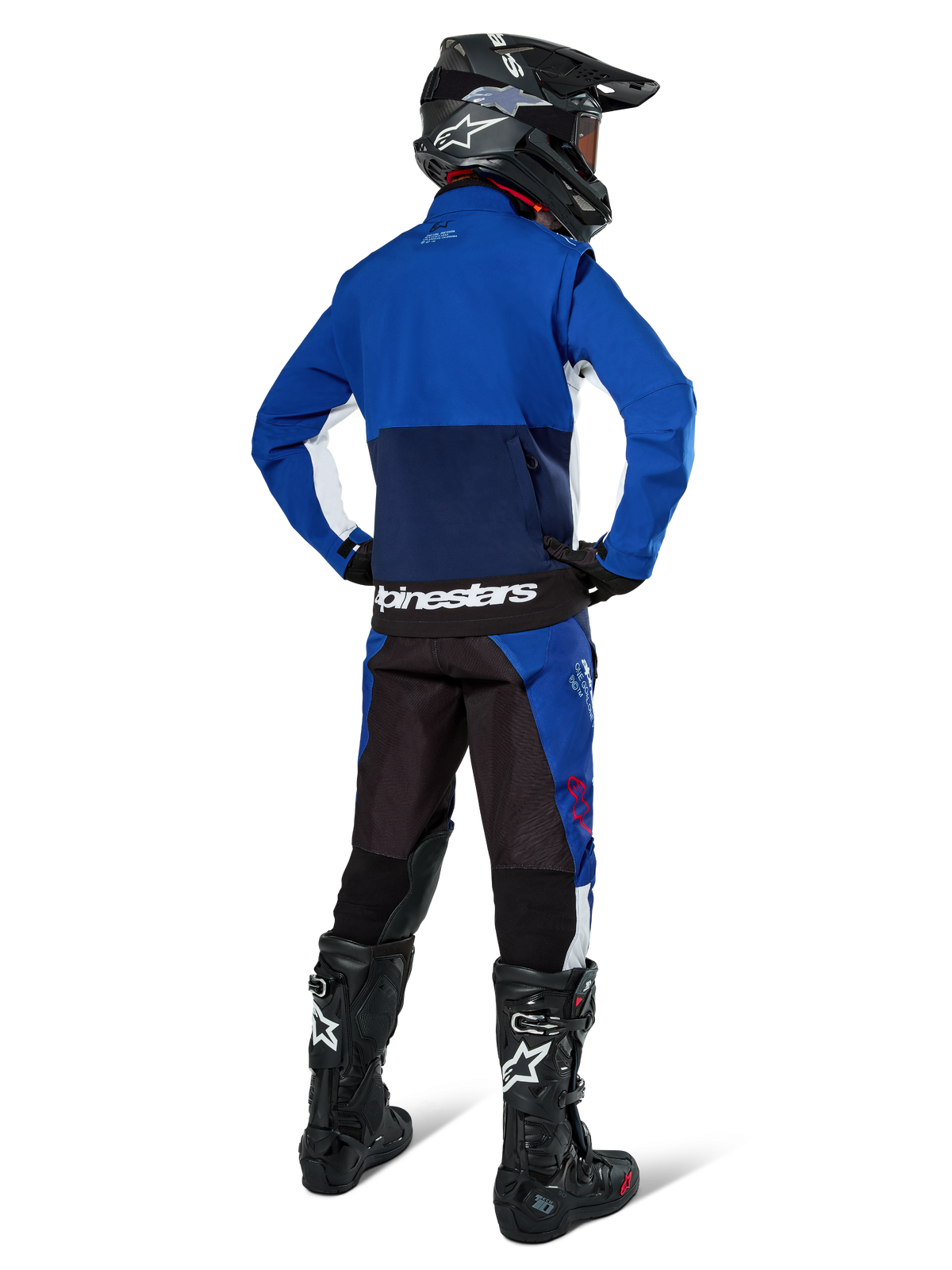 Motocross rider from behind wearing Alpinestars Lite-Dura Softshell Jacket in Navy Bright Blue and White, paired with matching enduro pants, black helmet, and black boots, complete off-road racing gear