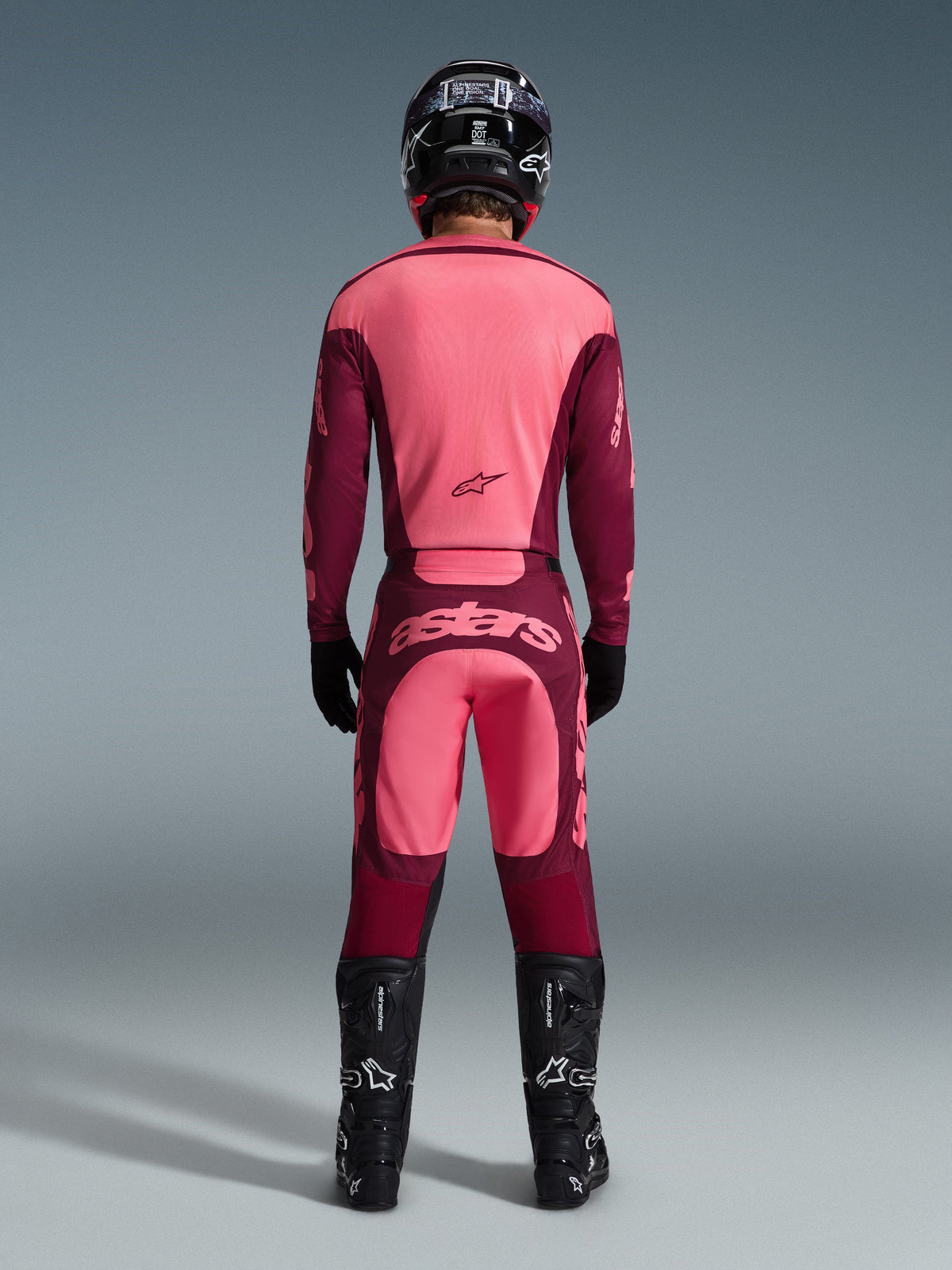 Motocross rider from the back wearing the Alpinestars 2026 Racer Riway Jersey and matching pants in Dark Red Coral, featuring black boots, a black helmet, and black gloves, coordinated high-performance gear for off-road racing