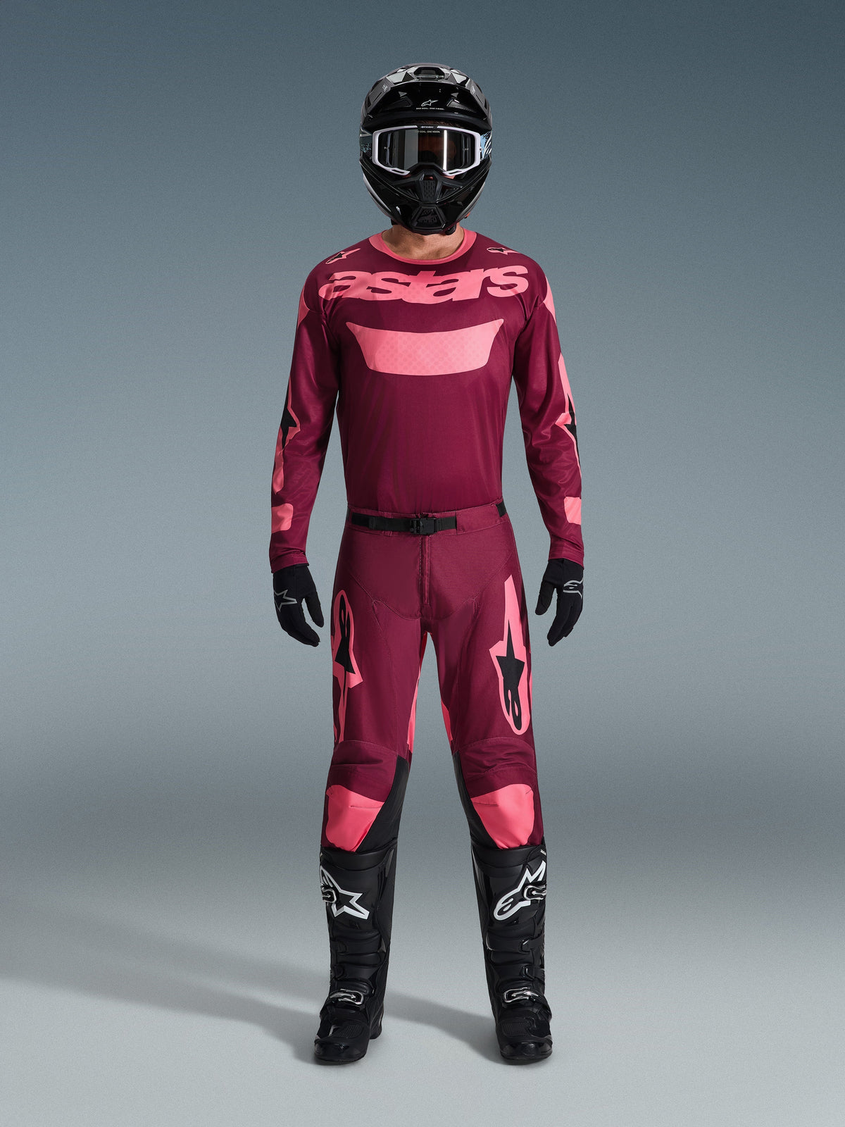 Motocross rider wearing complete racing gear, 2026 Racer Riway Jersey in Dark Red Coral, matching dark red pants with coral accents, black helmet with white accents, black boots with white logos, and black gloves, coordinated outfit for off-road racing