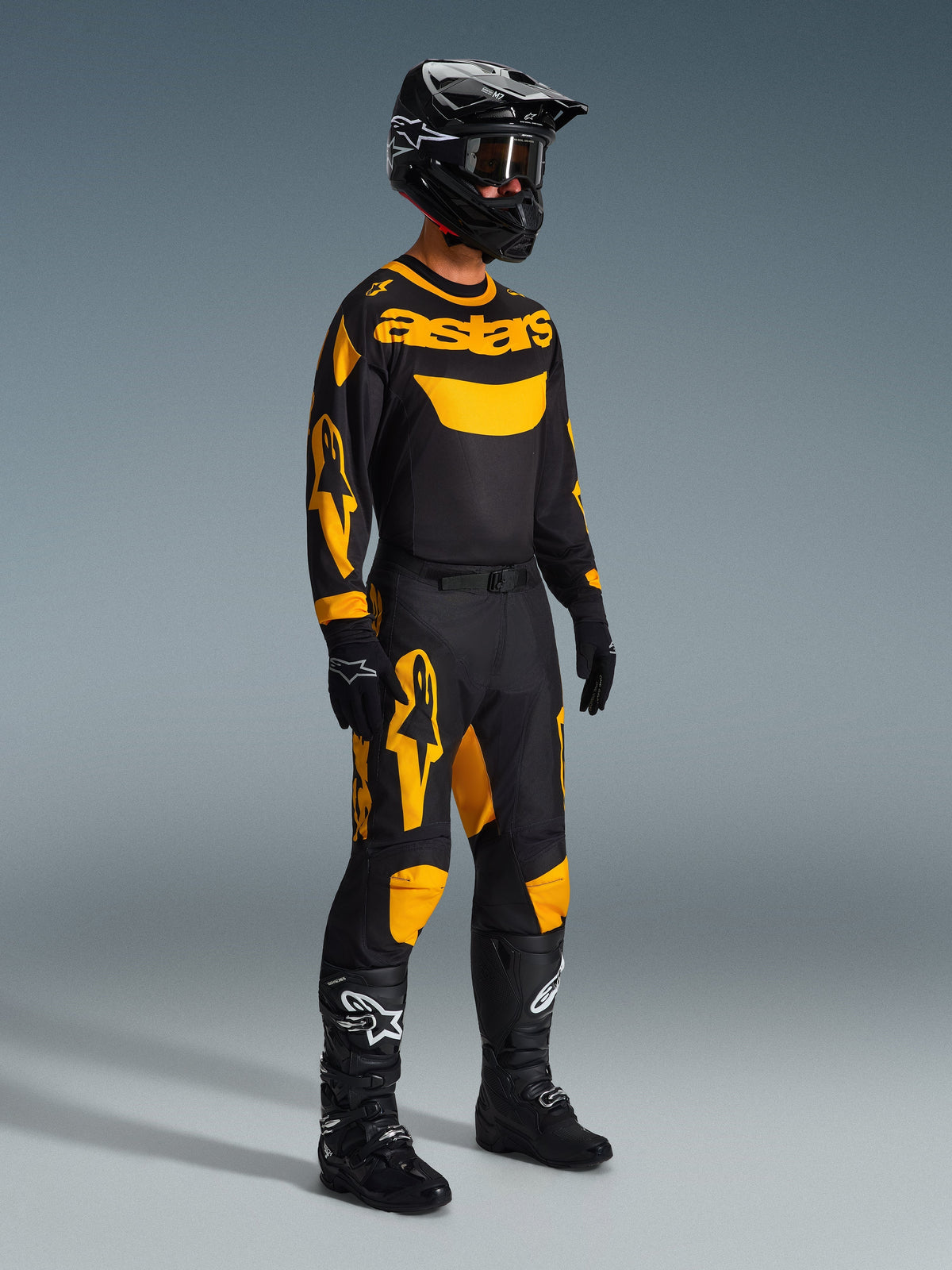 Motocross rider wearing the Alpinestars 2026 Racer Riway Pants in Yellow and Black, styled with a matching black and yellow 'astars' jersey, black helmet with goggles, and black racing boots, coordinated gear for off-road motocross performance.