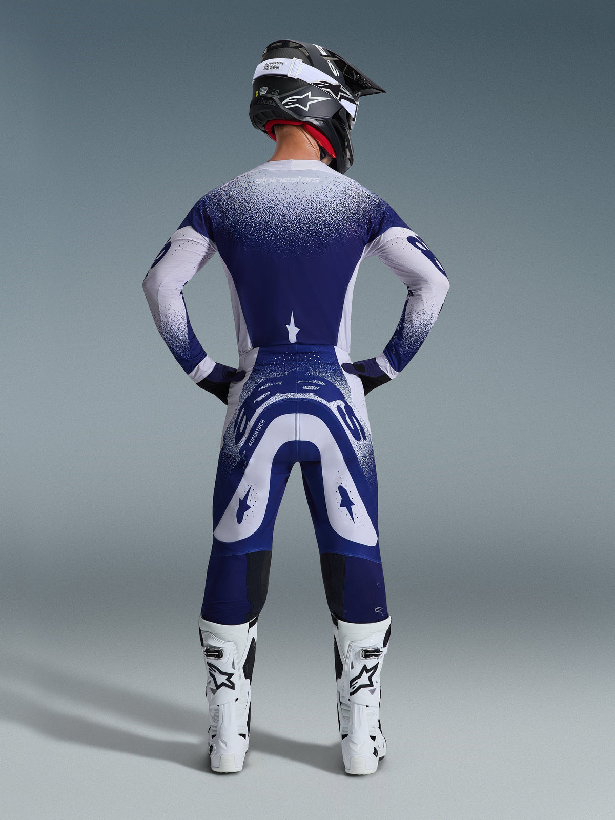 Alpinestars 2026 Supertech Scenz Pants, Motocross Pants, Light Gray and Dark Blue, rear view of a rider wearing a matching gear set with speckled gradient graphics, white boots and black helmet, professional athletic fit for off-road racing