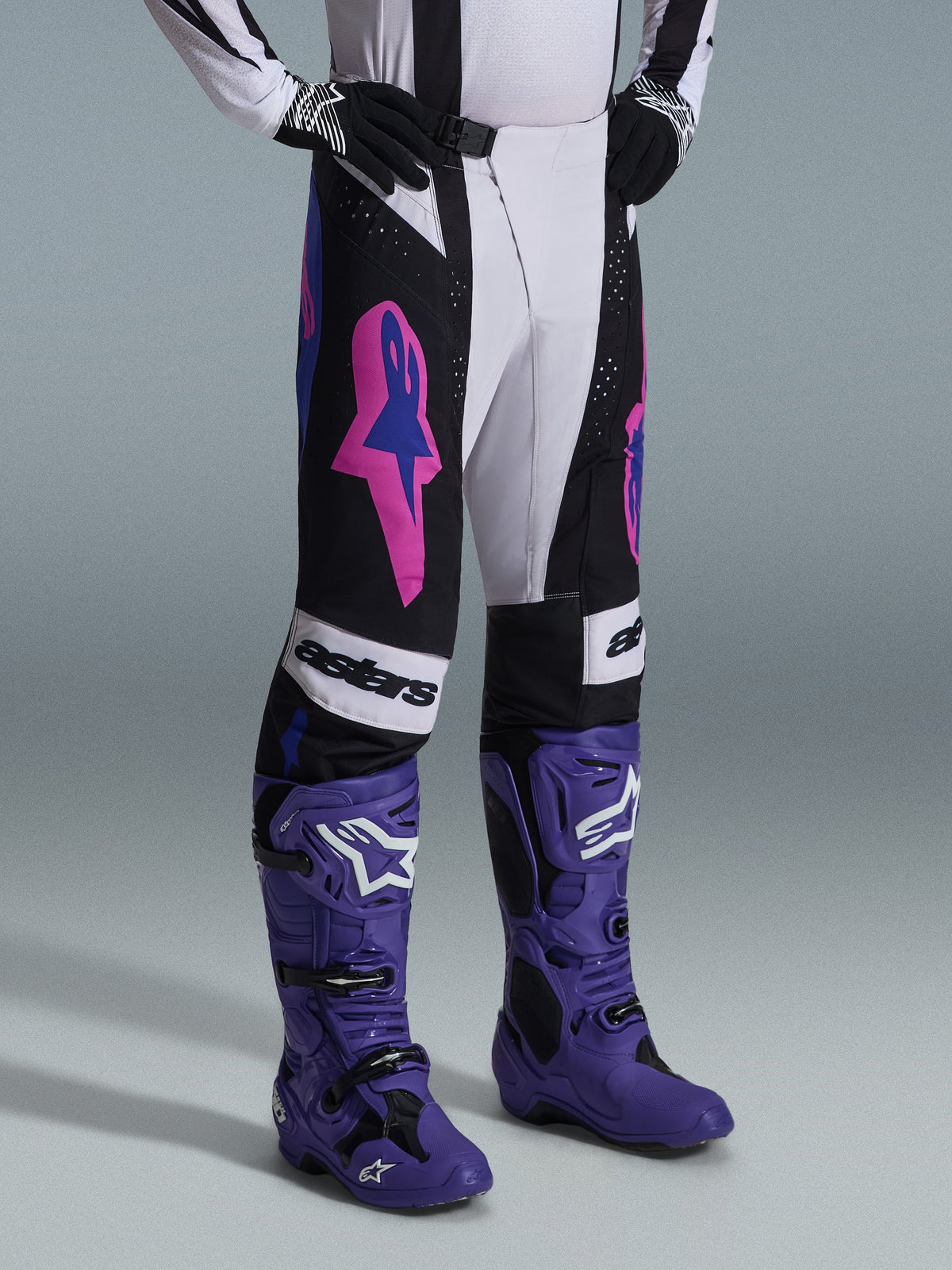 Alpinestars 2026 Techstar Knif Pants, Black Light Gray and Purple, worn with matching purple motocross boots, featuring bold pink accents and 'astars' branding, professional motocross racing gear