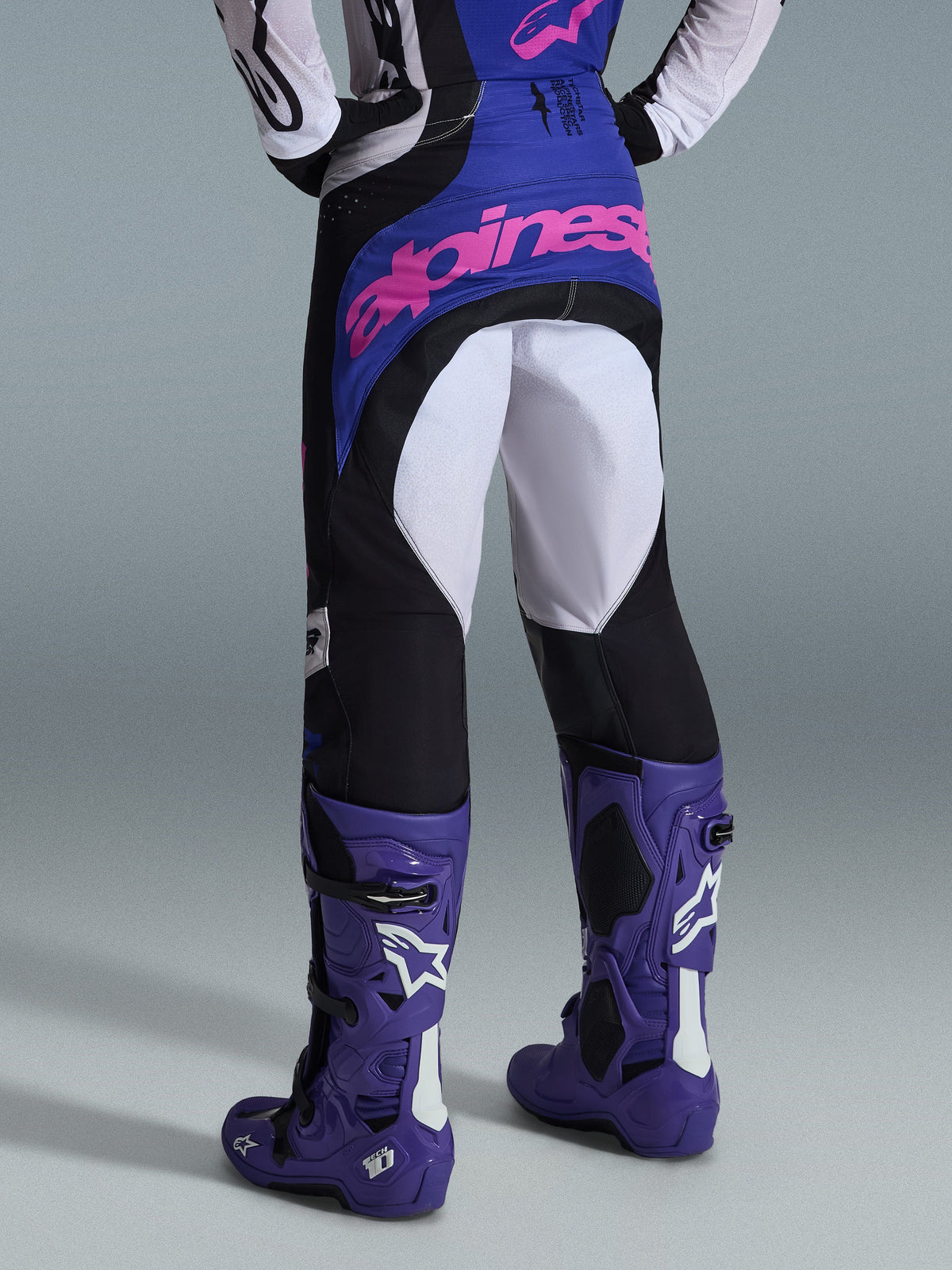 Alpinestars 2026 Techstar Knif Pants, Motocross Pants, Black Light Gray and Purple, rear view featuring pink branding on the seat, worn with matching jersey and purple motocross boots, professional off-road racing outfit