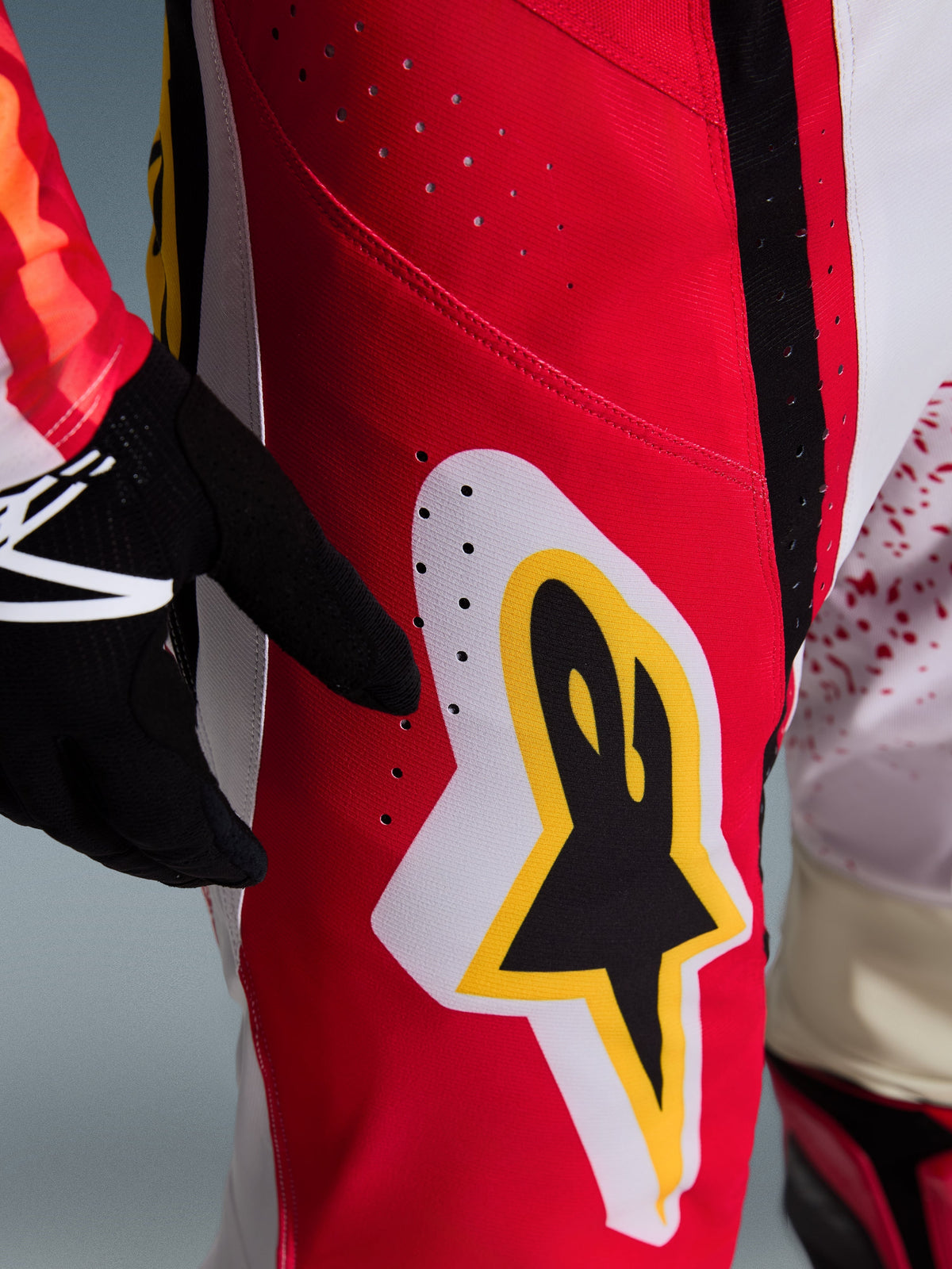 Alpinestars 2026 Techstar Nomur Pants, close-up of red and white panels on the thigh, featuring a large black, yellow, and white Astar logo, laser-cut perforations for ventilation, part of a professional motocross gear set.