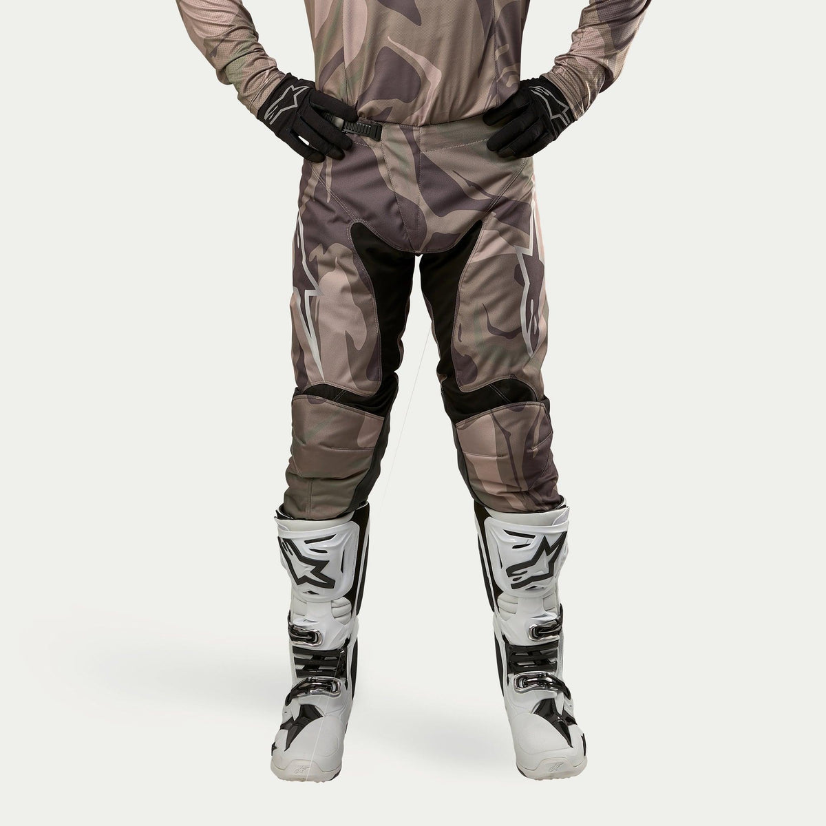 Alpinestars 2024 Racer Tactical Pants, Motocross Pants, Military Green Camo Brown, featuring large white Alpinestars logos on the thighs and black inner leg panels, worn with white and black motocross boots and black gloves, matching camouflage jersey, front view.