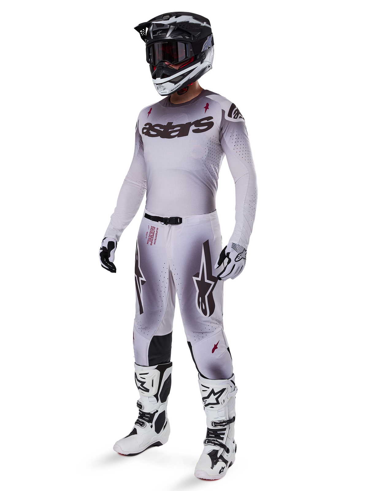 Motocross rider wearing complete racing gear, grey and white gradient jersey with black 'astars' branding, matching pants with red accents and star logos, black and white helmet with dark goggles, white Alpinestars Tech 10 Boots, professional off-road racing outfit