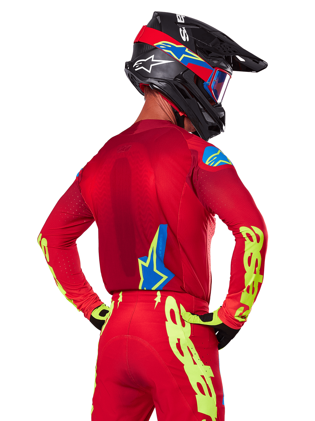 Rear view of a motocross rider wearing the Alpinestars 2025 Supertech Maker Gear Set in Red, featuring a red jersey with neon yellow branding on the sleeves, matching red pants, a black helmet with blue and red accents, and coordinating black and yellow gloves.