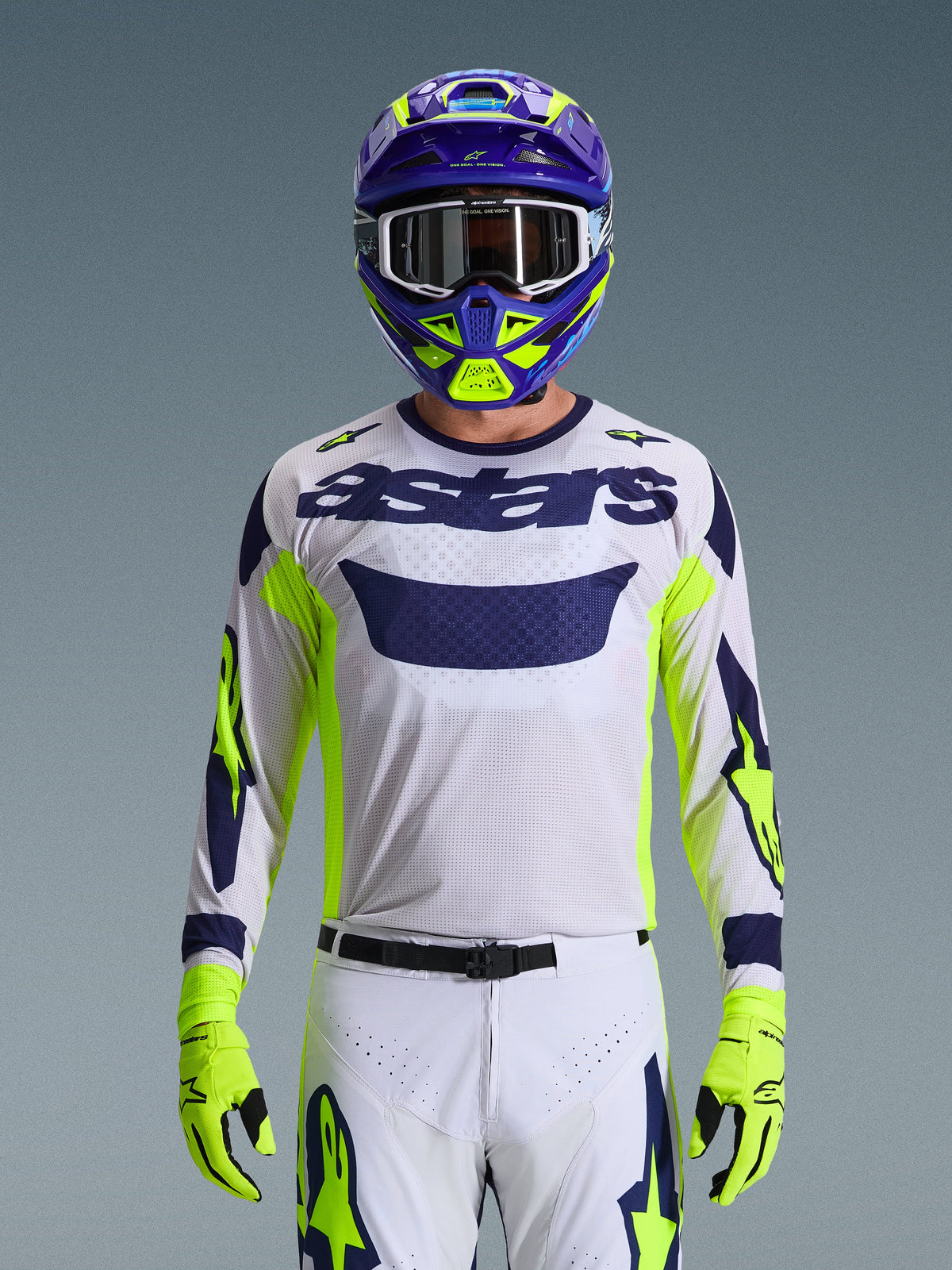 Motocross rider wearing the Alpinestars 2026 Racer Air Riway Gear Set, white mesh jersey with navy blue 'astars' branding and fluo yellow accents, matching white pants with navy and fluo yellow graphics, fluo yellow gloves, purple and fluo yellow helmet with white goggles, studio shot showing a complete off-road racing kit