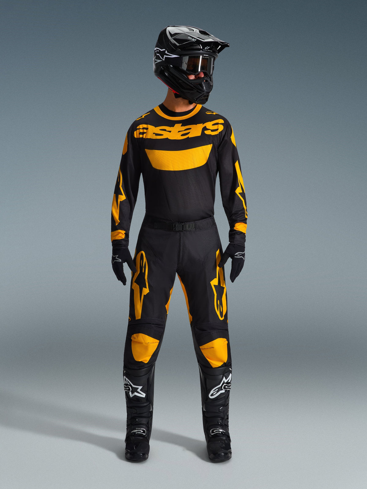 Motocross rider wearing the 2026 Racer Riway Jersey in Yellow and Black, coordinated with matching pants, black helmet, and black boots with white Alpinestars logos, full gear set for off-road racing.