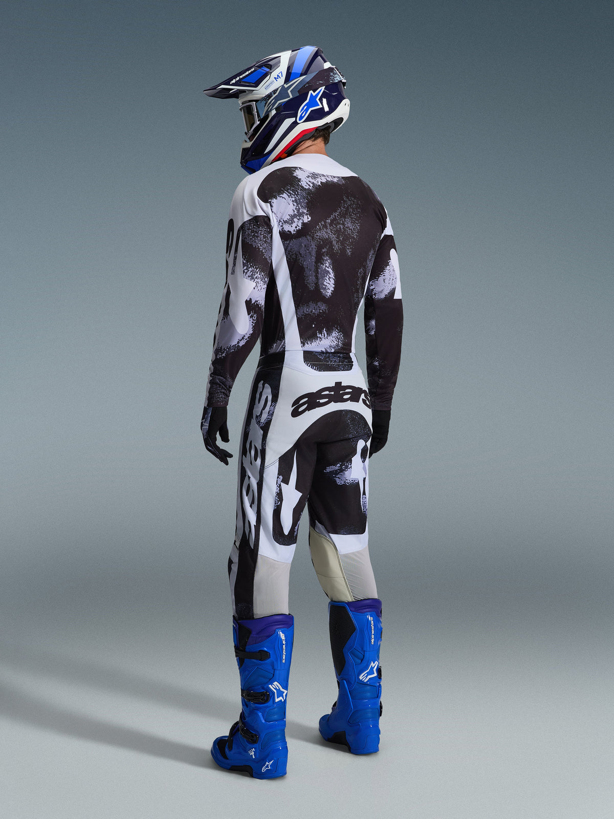 Alpinestars 2026 Racer Lahnd Gear Set, rear view of motocross rider wearing black and white abstract pattern jersey and pants, blue motocross boots and helmet, professional racing kit for off-road performance