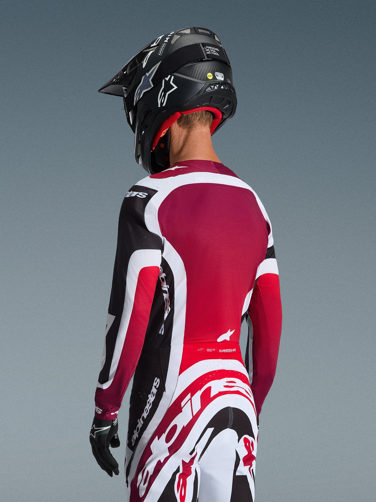 Rear view of a motocross rider wearing the 2026 Supertech AFD Vista Jersey in Black Red and White, coordinated with matching pants and a black helmet, featuring bold Alpinestars branding, red mesh panels, and an athletic racing fit.