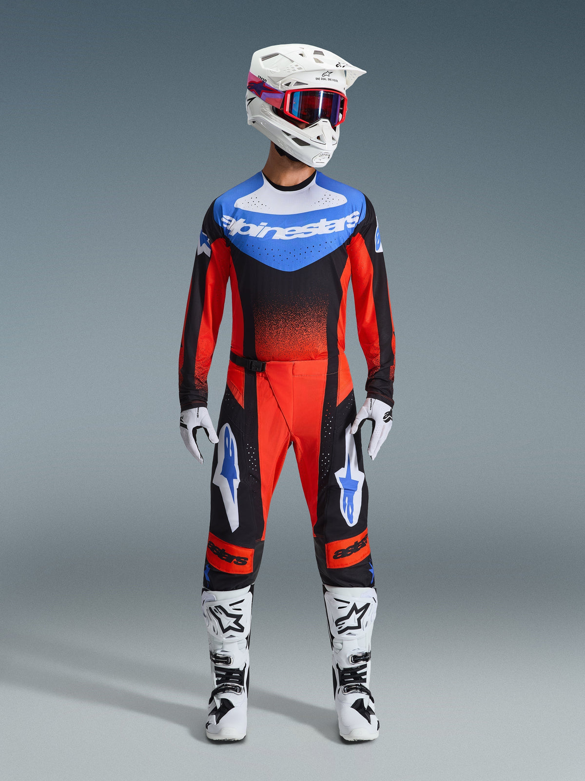 Motocross rider wearing complete racing gear, 2026 Techstar Knif Jersey in Orange Black and UCLA Blue, matching motocross pants, white helmet with goggles, white gloves, and white boots, coordinated Alpinestars outfit for off-road competition