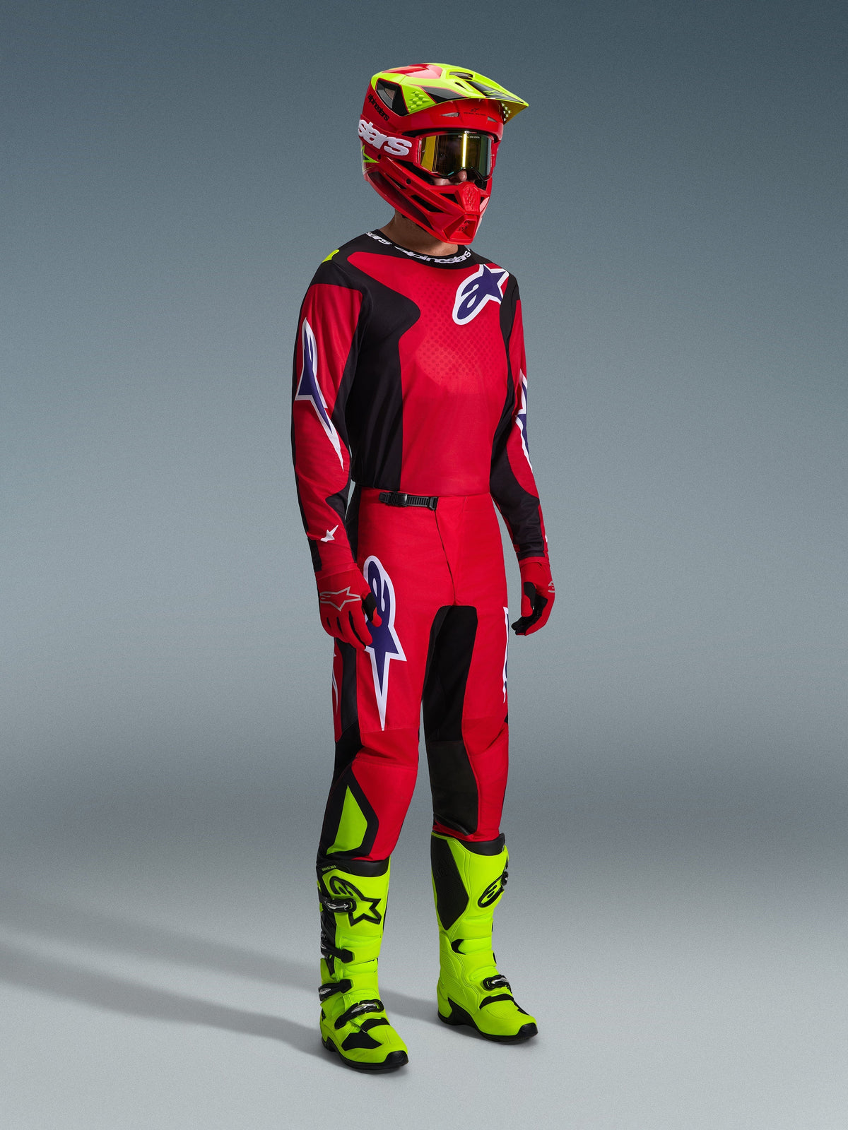 Motocross rider wearing the Alpinestars 2026 Fluid Grid Gear Set in Red Black and Purple, featuring a matching jersey and pants with purple logos, a red and neon yellow helmet, and neon yellow boots for a complete off-road racing kit.