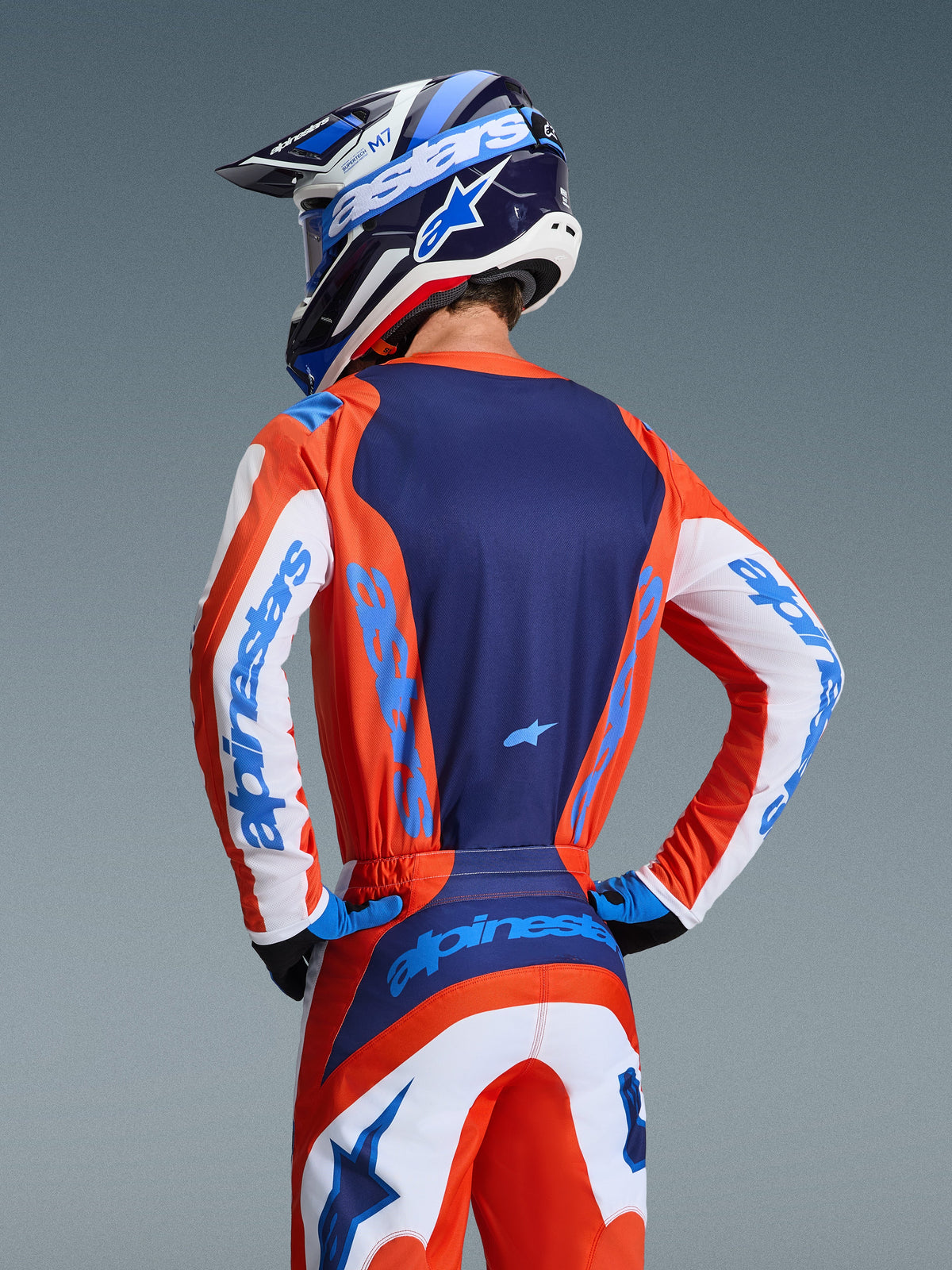 Alpinestars 2026 Fluid Grid Jersey, Rear view of motocross rider wearing coordinated Orange and UCLA Blue gear set, navy blue back panel, white sleeve accents with blue branding, matching helmet, performance off-road apparel