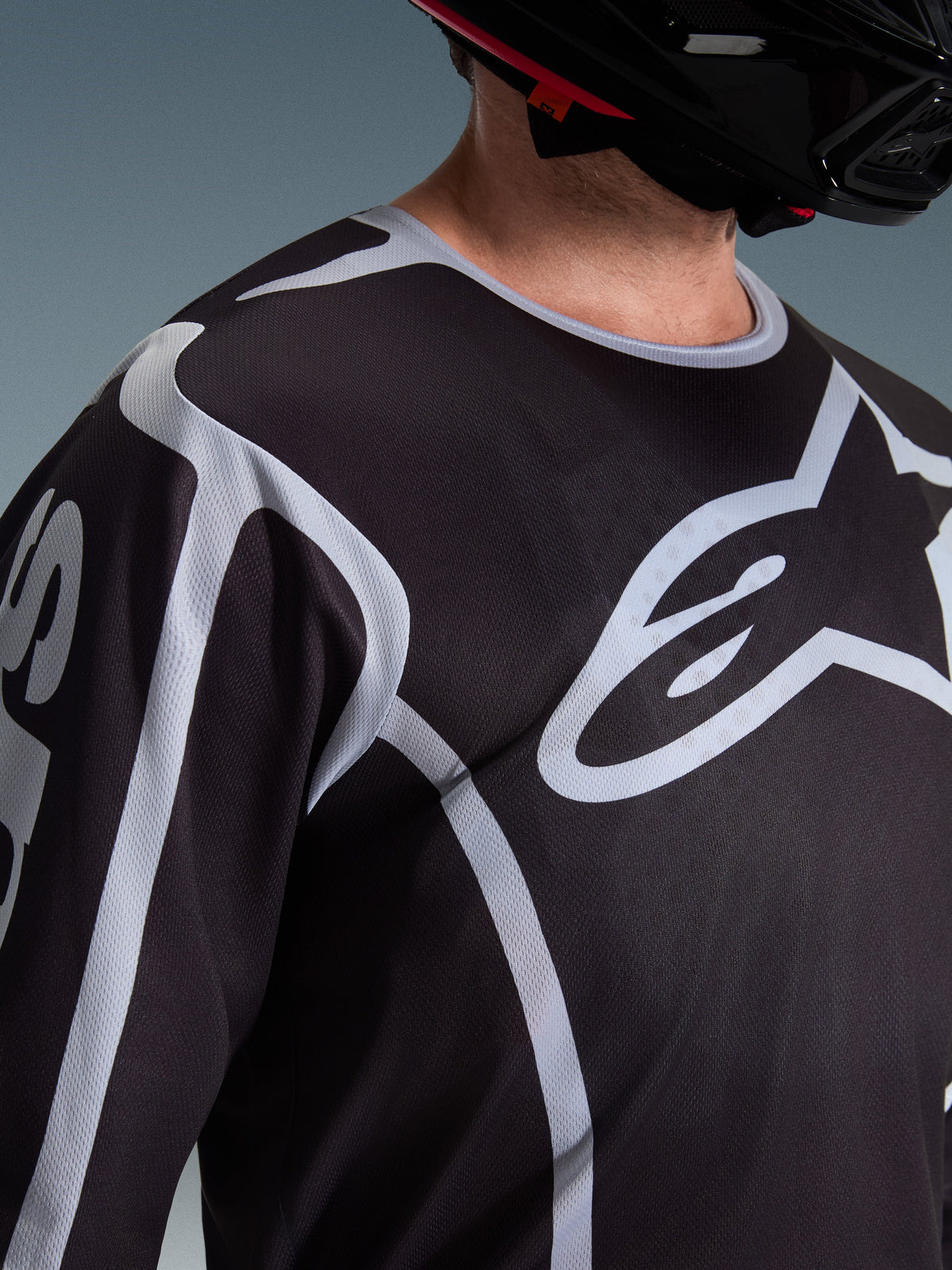 Alpinestars 2026 Fluid Apex Jersey, Motocross Jersey, Black and Grey, featuring large Alpinestars logo on the chest, sport collar, worn with a black helmet, performance gear for off-road riding