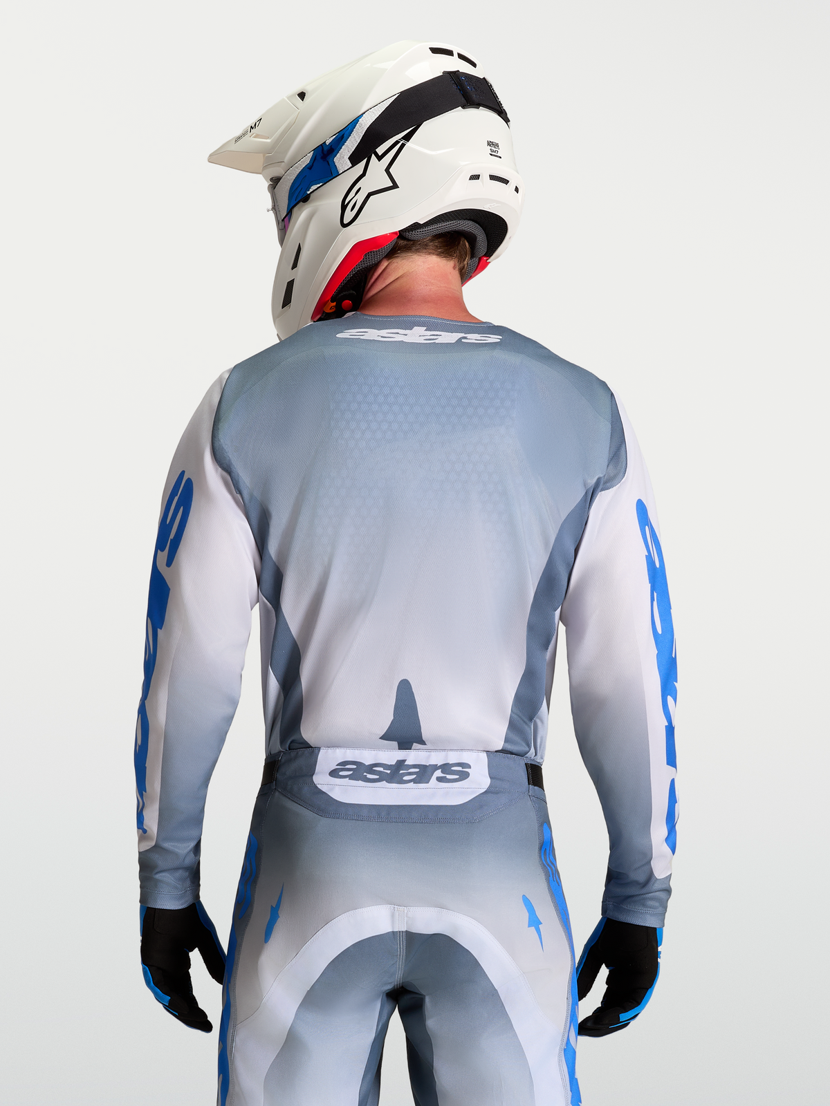 Alpinestars Racer Amber Jersey, Gray and White Motocross Jersey, Ash Gray moisture-wicking polyfabric with light lilac and UCLA blue graphics, ergonomic race fit, on-model rear view with white helmet.