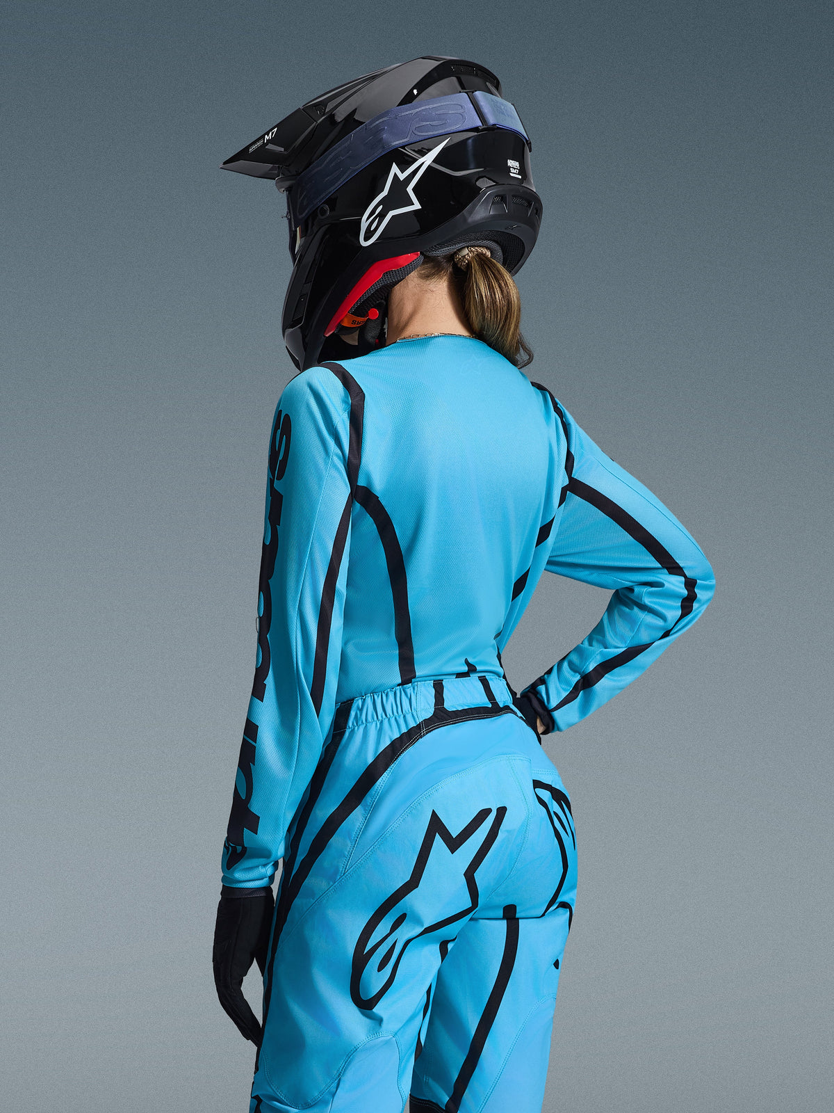 Alpinestars 2026 Stella Fluid Apex Gear Set, Light Blue and Black, back view of a female rider wearing a motocross jersey and matching pants, black Alpinestars helmet with white logo, technical off-road racing apparel for women.