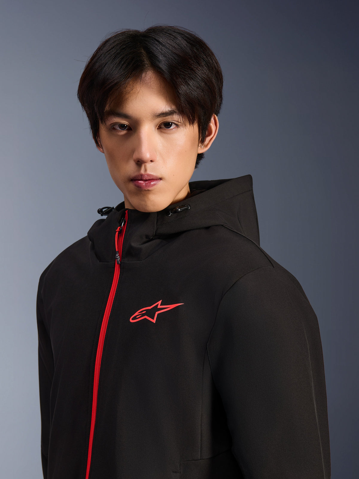 Alpinestars Radium Tech Hoodie, Urban Motorcycle Jacket, Black and Bright Red, male model wearing a technical shell hoodie featuring a bright red front zipper and chest logo, modern urban riding design