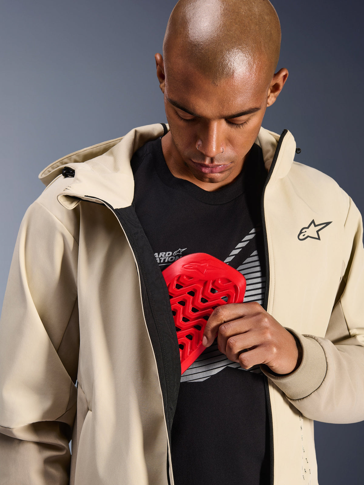Alpinestars Radium Tech Hoodie in Mastic Aluminum, Urban Motorcycle Jacket, model demonstrating internal armor pocket with a red Nucleon chest protector, windproof tech shell with a casual hoodie design and Alpinestars branding.