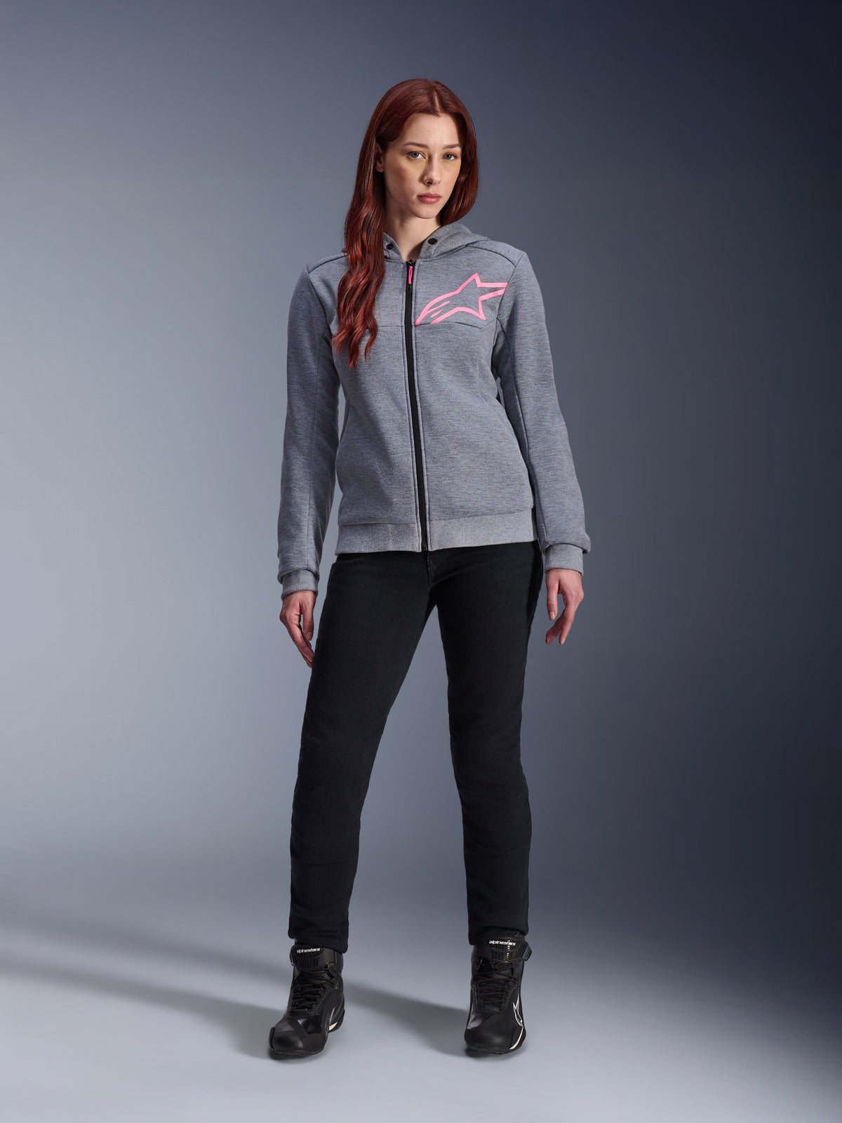 Alpinestars Stella Chrome V2 Sport Hoodie, Gray Heather Pink Fluo, worn by a woman with black pants and boots, featuring a pink Alpinestars star logo on the chest, full-zip urban motorcycle gear, lightweight tech fleece with a casual athletic fit.