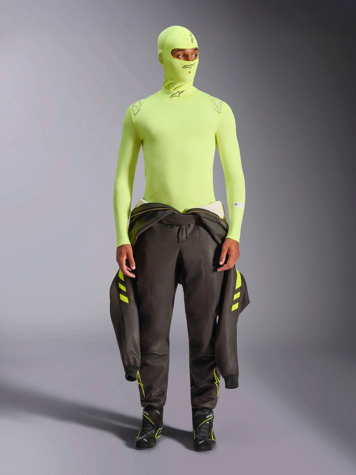 Alpinestars ZX Evo V3 Long Sleeve Top, Yellow Fluo, worn with matching balaclava and dark racing suit tied at waist, lightweight flame-resistant base layer for auto racing, featuring Alpinestars logos on the collar and shoulders