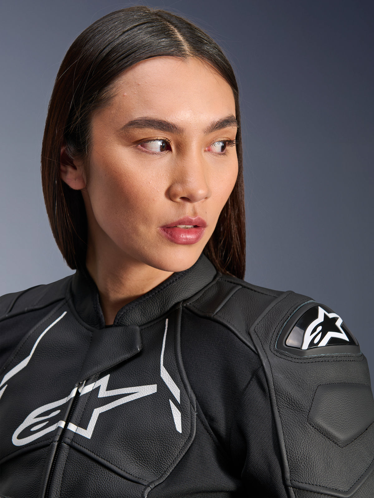 Woman wearing the Alpinestars Stella Dusk Leather Jacket in Black and White, close-up portrait featuring the white Alpinestars chest logo and external DFS shoulder protector, premium leather construction for motorcycle road racing