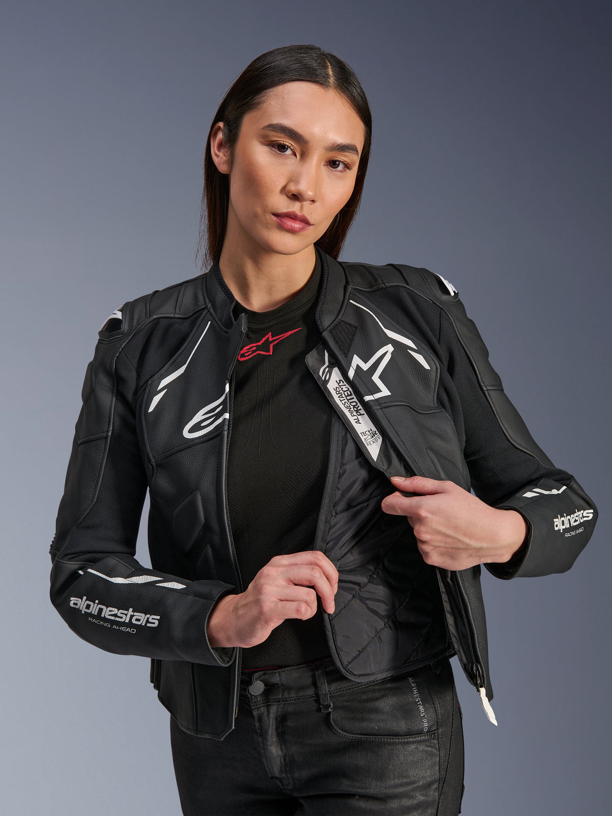 Female model wearing the Alpinestars Stella Dusk Leather Jacket in Black and White, showcasing the internal quilted thermal liner and Tech-Air Ready label, premium bovine leather with white star logo and 'RACING AHEAD' sleeve branding